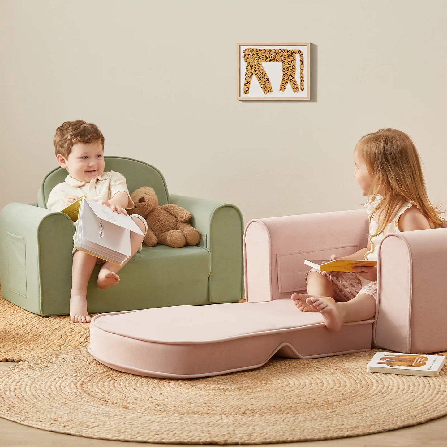 Two children sitting on green and pink Tiny Land® GentleSnug Kid Chair with a teddy bear and books in a cozy room.
