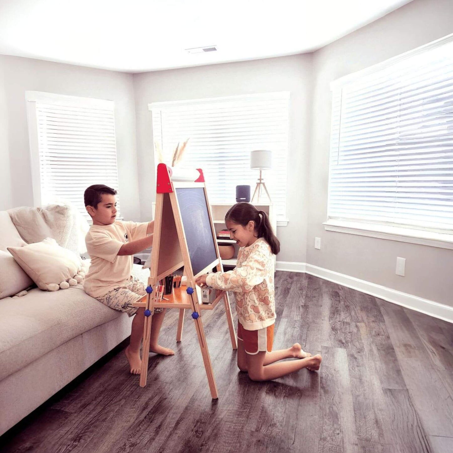 Two children painting on Tiny Land® 3-in-1 Art Easel & Paper Roll Set in a modern living room.