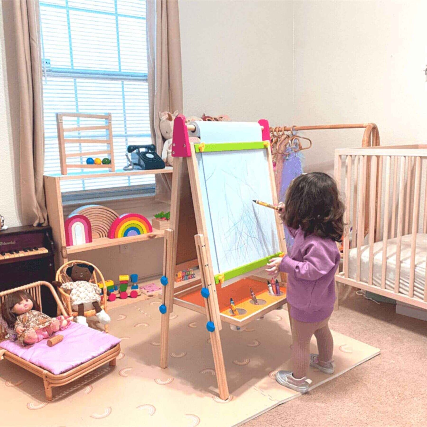 Child drawing on Tiny Land® 3-in-1 Art Easel & Paper Roll Set in a nursery with toys and furniture around