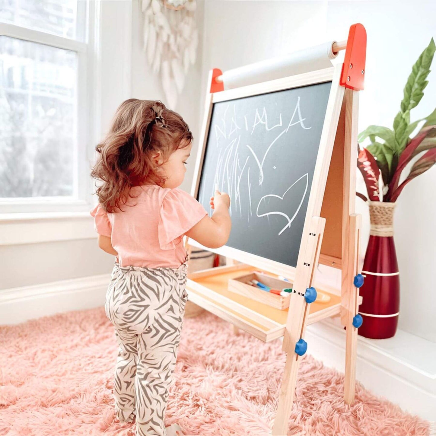 Child drawing on Tiny Land® 3-in-1 Art Easel & Paper Roll Set with a chalk marker in a bright room.