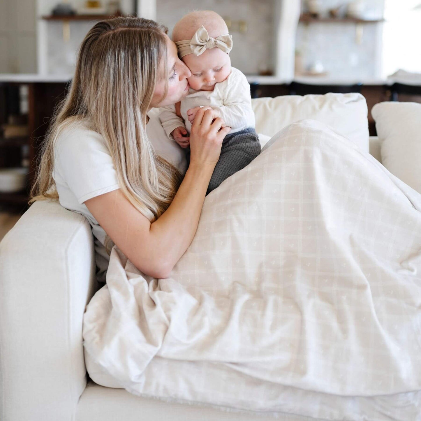 Woman holding a baby wrapped in Saranoni Minky/Lush Throw Blankets - Ivy on a couch