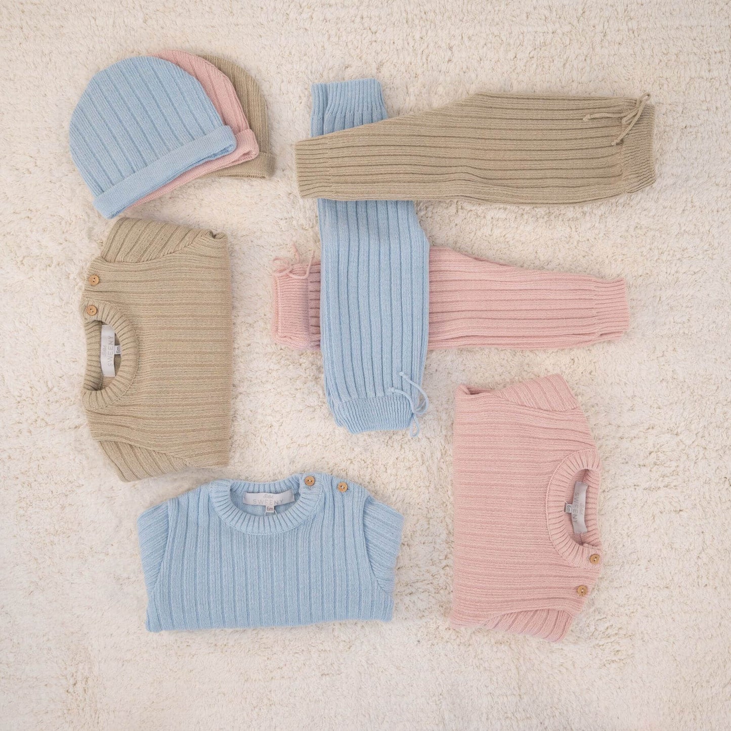 Collection of pastel-colored baby clothes on a soft beige surface