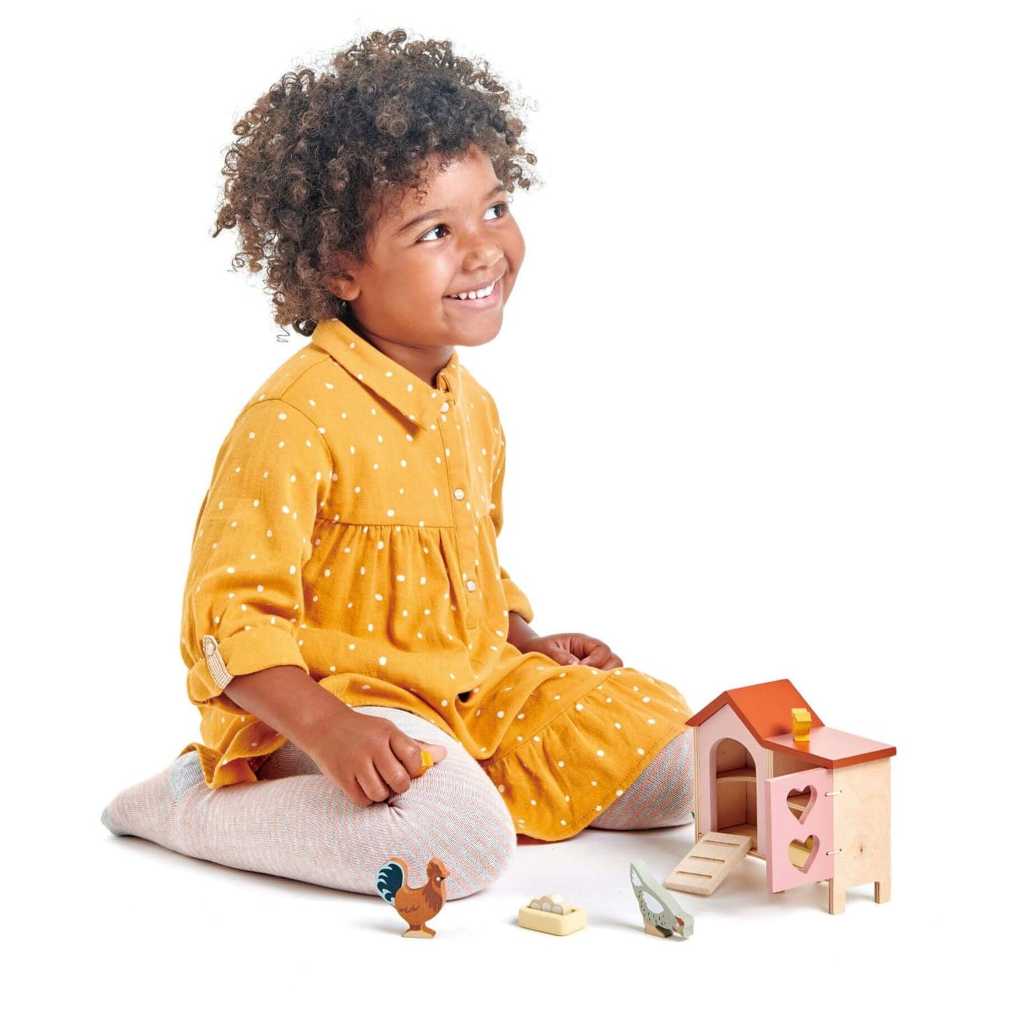 Child in a yellow dress playing with a toy chicken and house on a white background