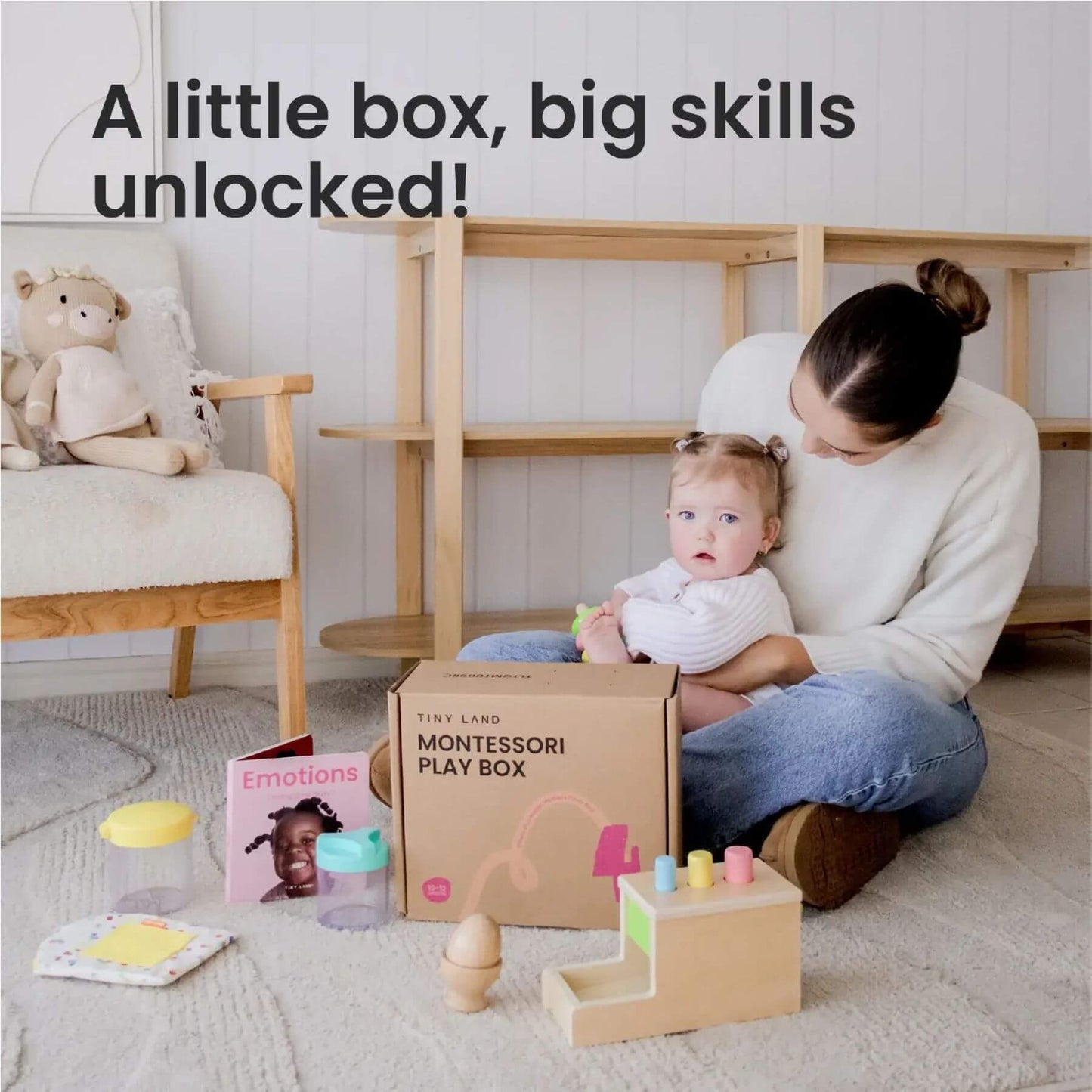 Woman holding a baby with Montessori play items and a box labeled 'Montessori Play Box' in a home setting.