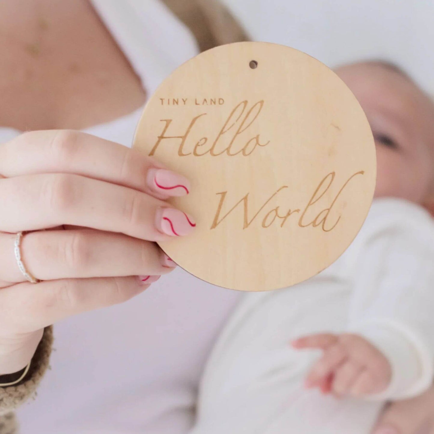 Wooden disc with 'Hello World' text held by a person with a baby in the background