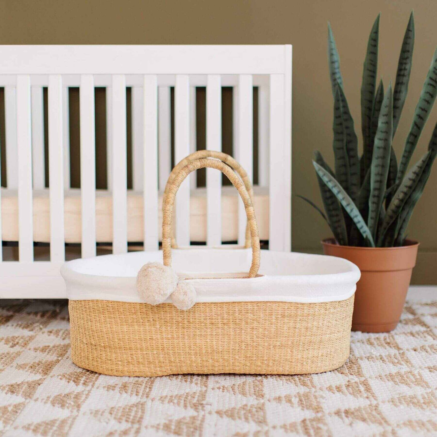 African Moses Basket No Hood Vegan Handle with white lining on a checkered floor in front of a white crib.