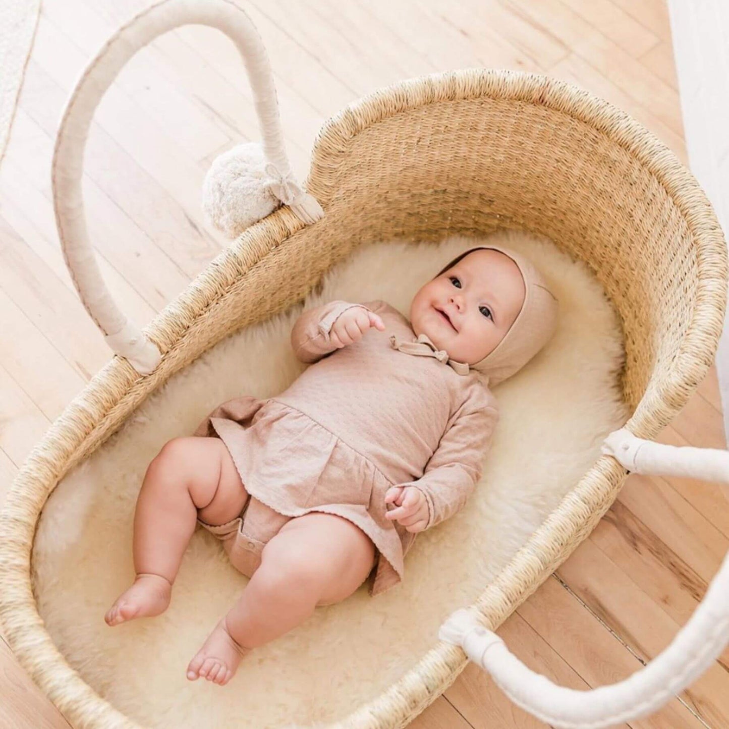 Baby lying in Plum+Sparrow African Moses Basket Cream Handle on a wooden floor