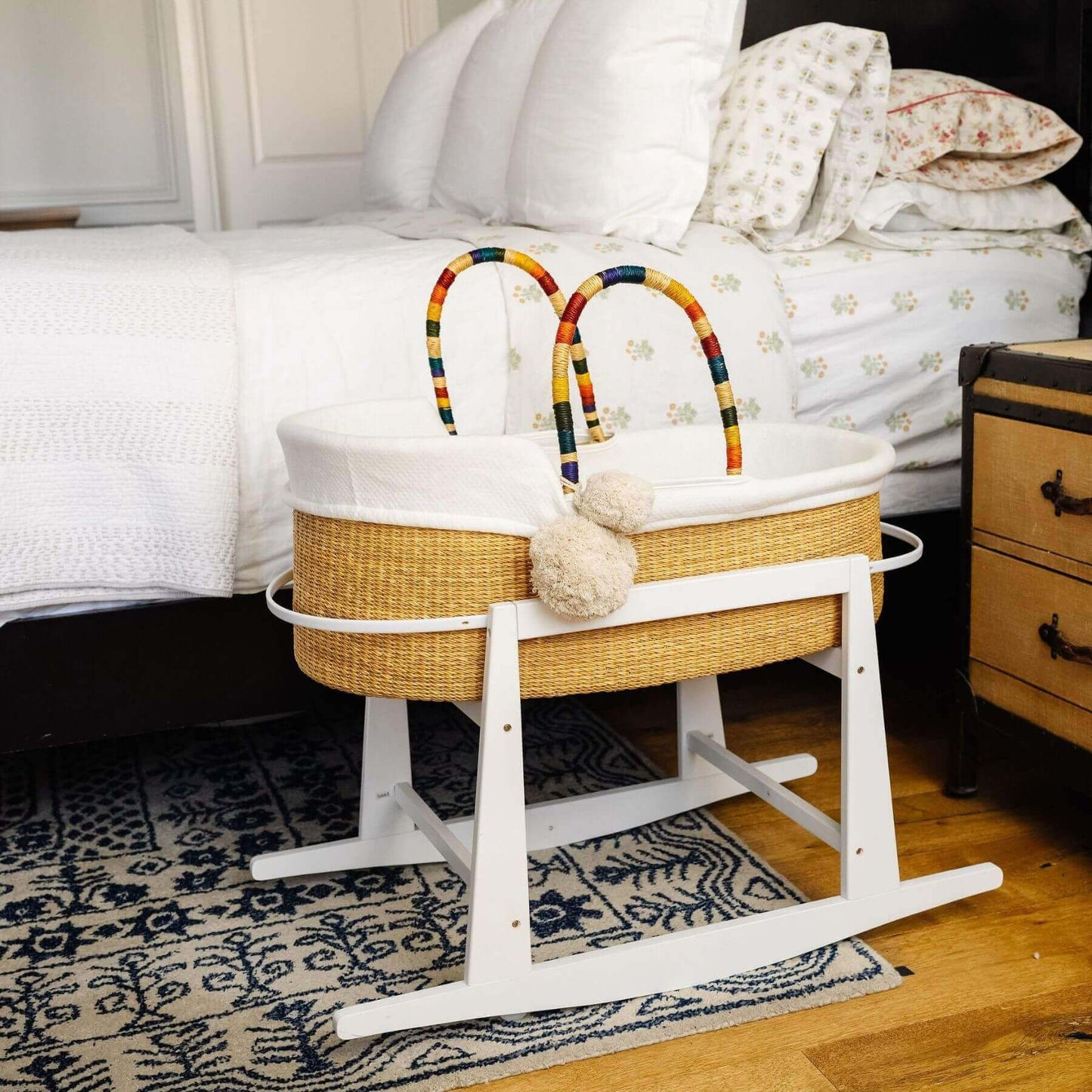 Plum+Sparrow Rainbow Handle Moses Basket on a stand in a bedroom setting.