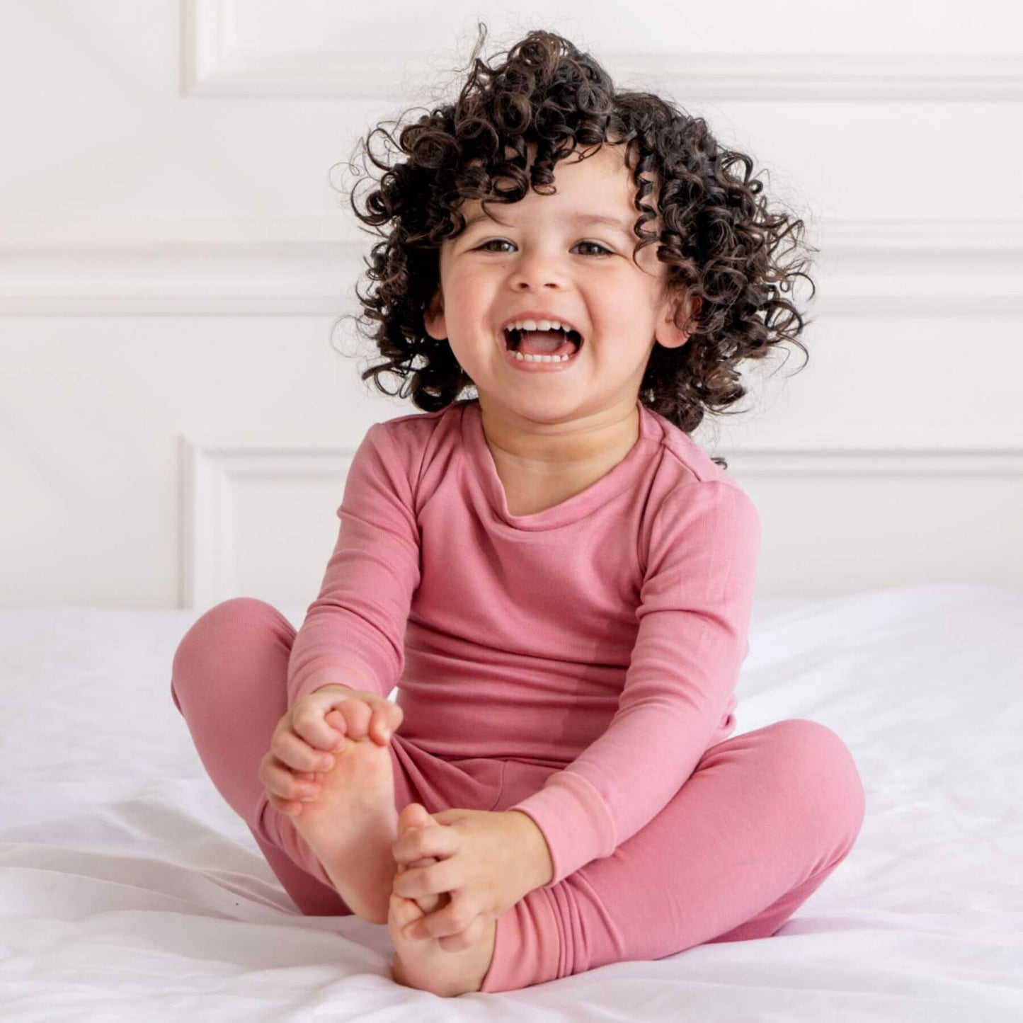 Child wearing Dreamland Baby Toddler/Kids Bamboo Pajamas - Dusty Rose sitting on a bed
