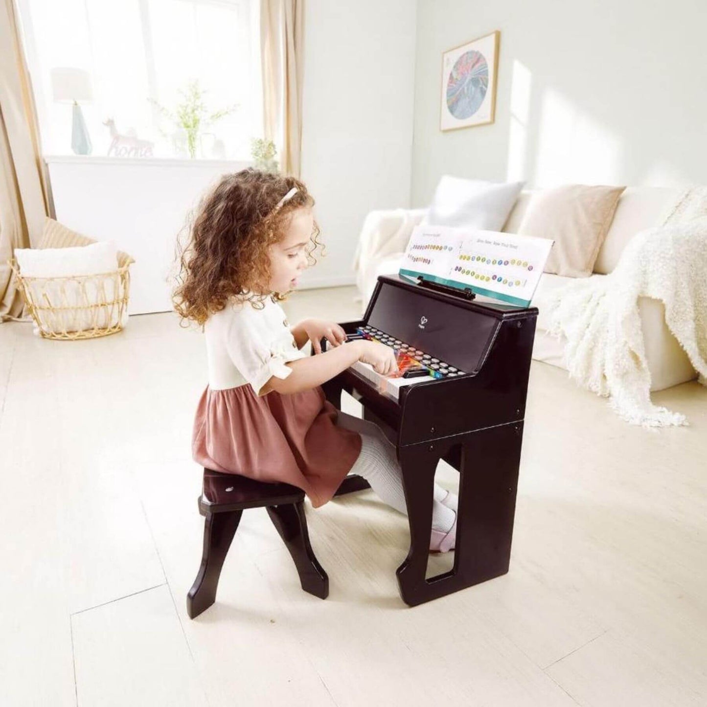 Child playing Hape Learn with Lights Black Piano w/ Stool in a bright room with a couch and decor.