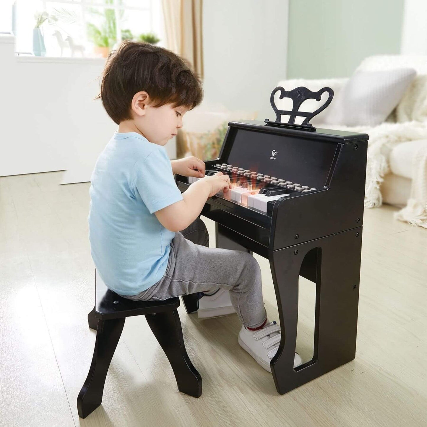 Child playing Hape Learn with Lights Black Piano w/ Stool in a bright room.