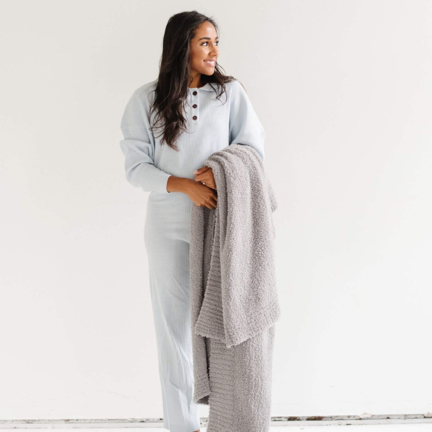 Woman holding Saranoni Bamboni® Throw Blanket in a light gray outfit against a white background