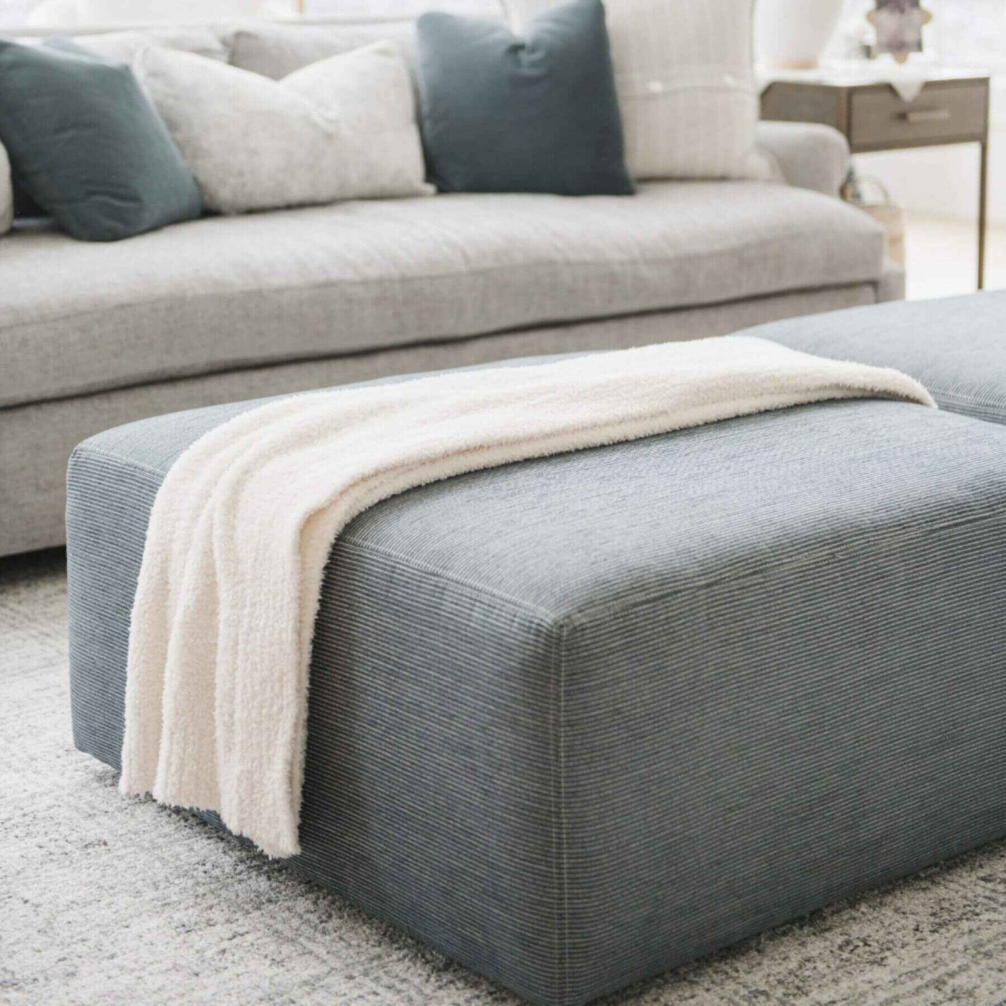 Gray ottoman with Saranoni Bamboni® Throw Blanket on top, in a living room setting.