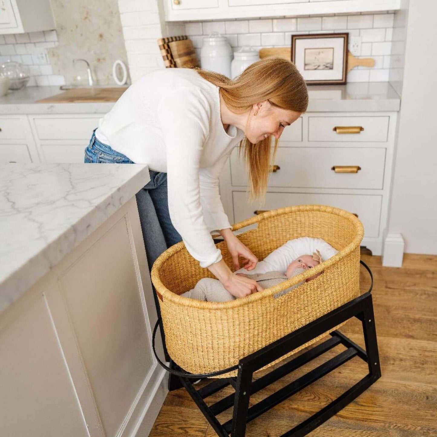 Woman adjusting a baby in African Moses Basket No Hood Inset Handle in a kitchen.