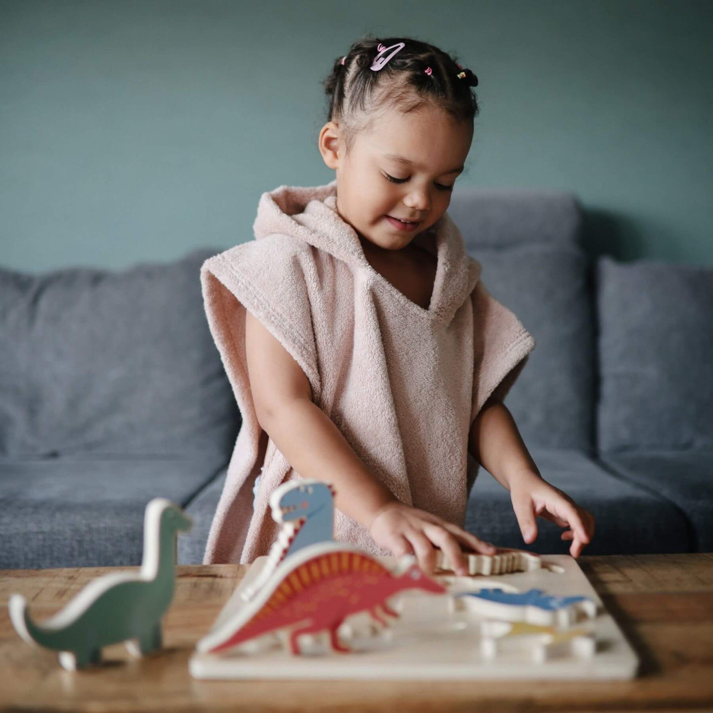 Child in Mushie Bear Poncho Towel playing with wooden dinosaur toys on a table