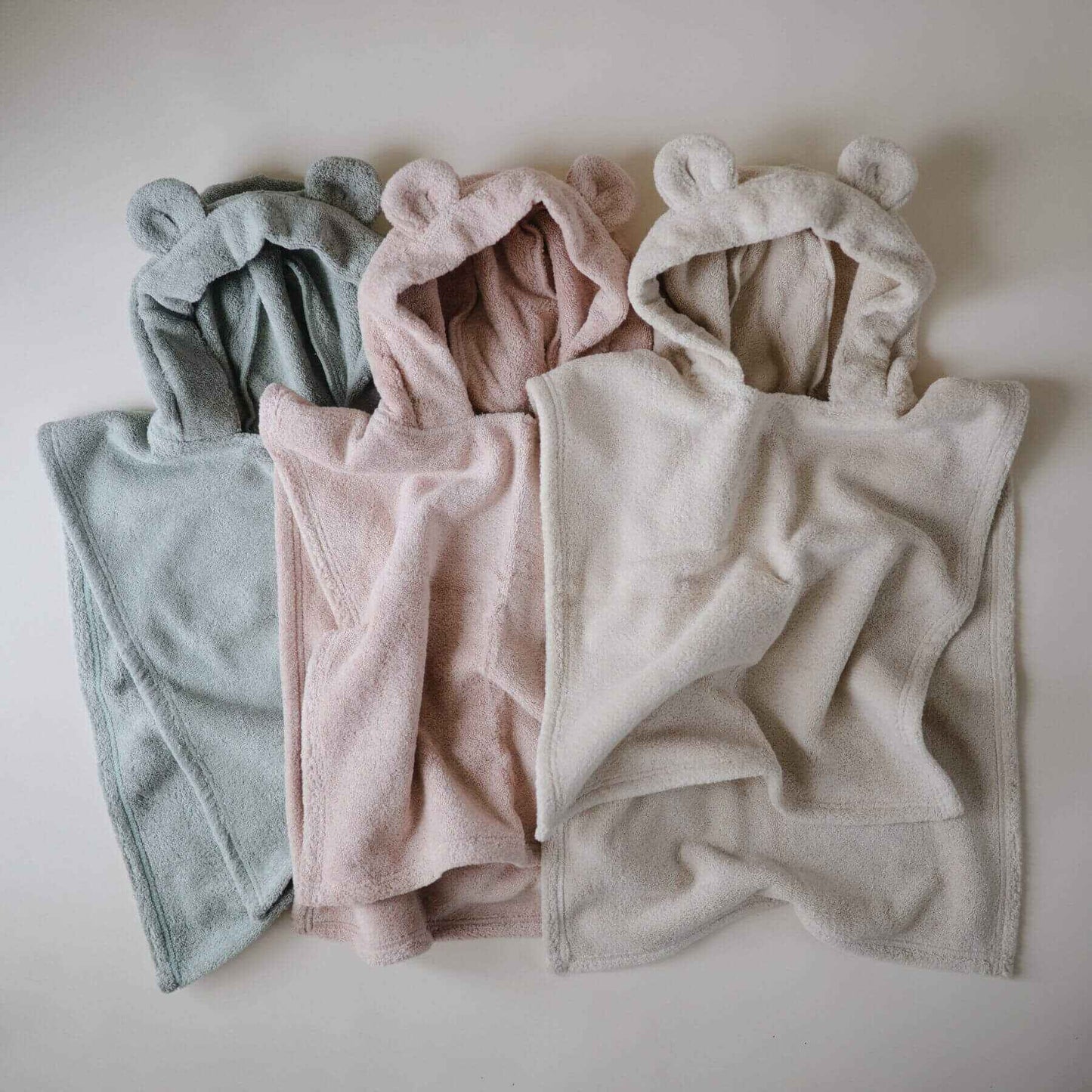 Mushie Bear Poncho Towels in different colors arranged on a light background