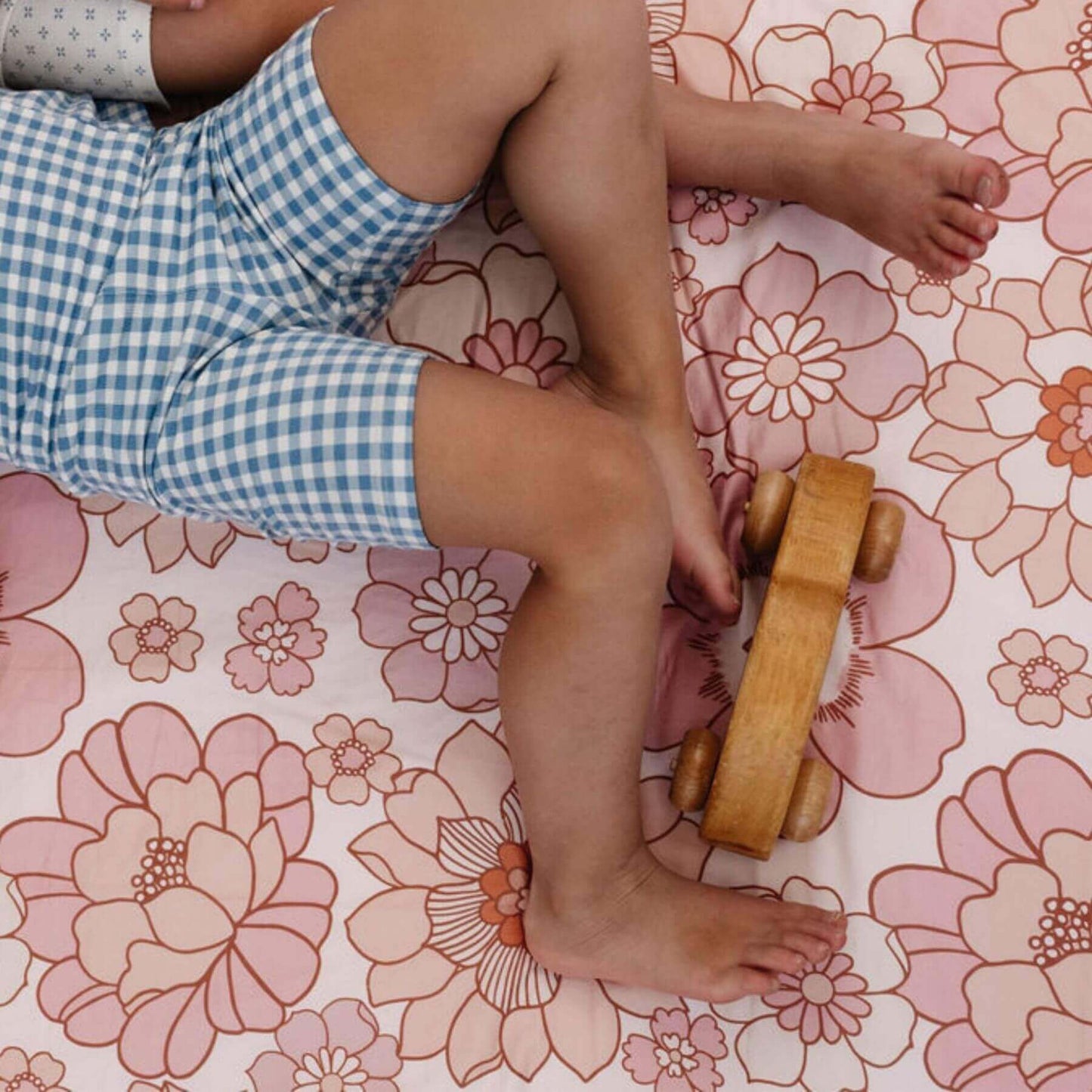 Child's legs and feet on aToki Mats Blooms Organic Cotton Mat with a wooden toy car.