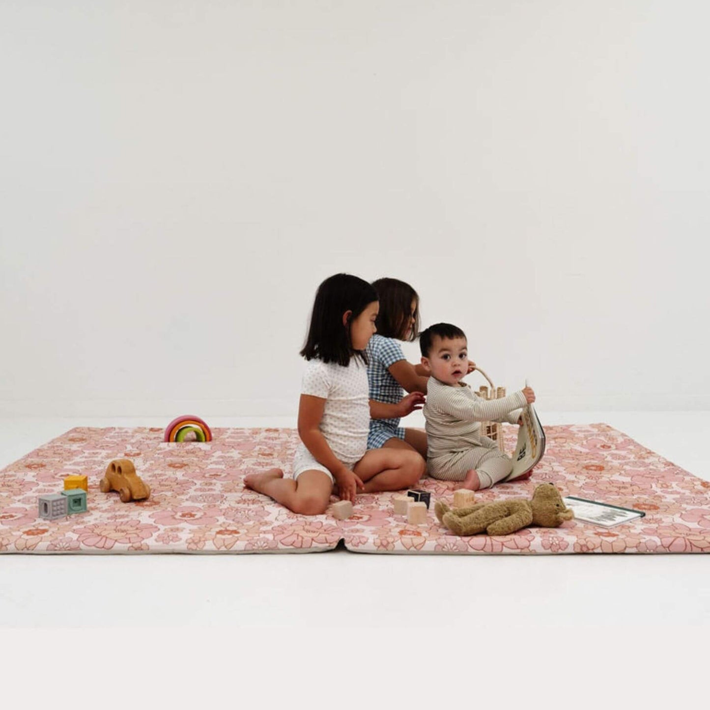 Three children playing on Toki Mats Blooms Organic Cotton Mat with toys against a white background
