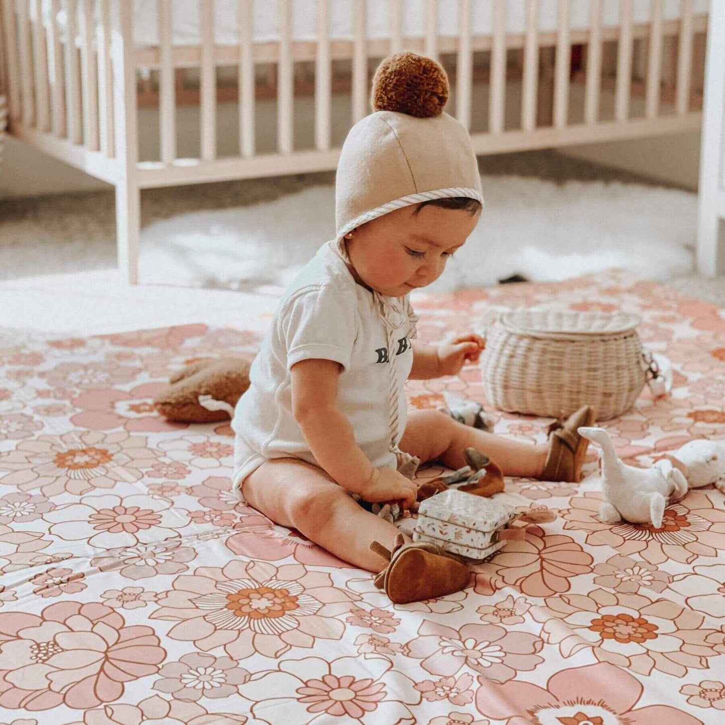 Child playing on Toki Mats Blooms Organic Cotton Mat in a nursery with a crib in the background