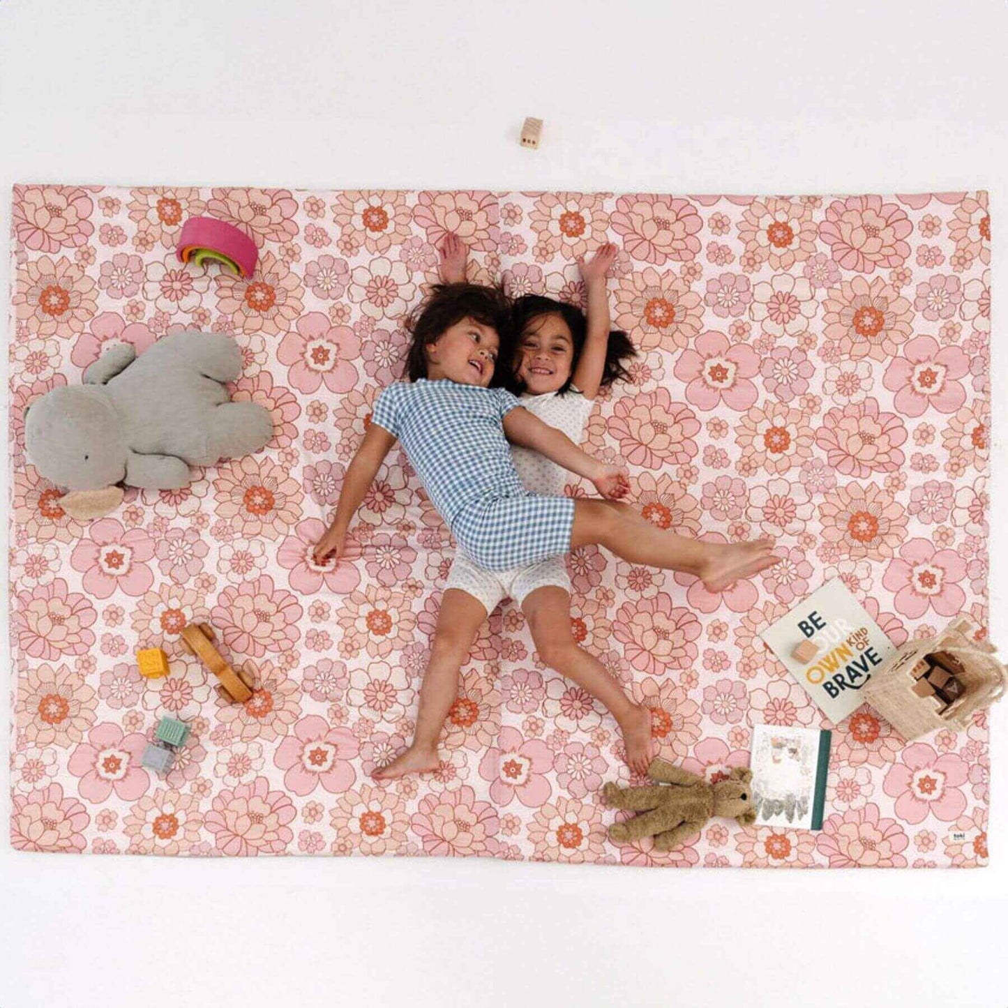 Two children lying on Toki Mats Blooms Organic Cotton Mat with toys around