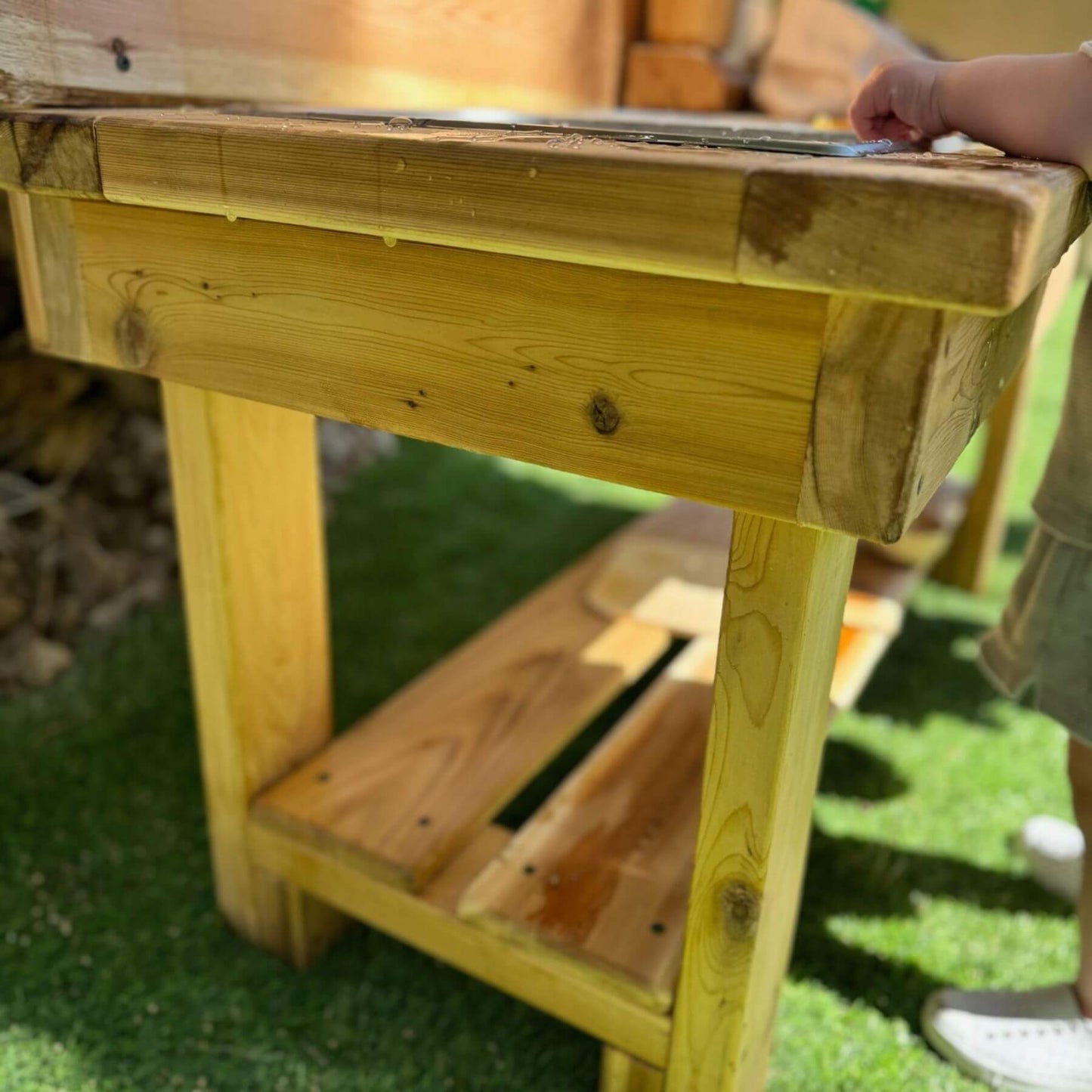 Bunny Hopkins Mud Kitchen with a child's hand on it, outdoors.