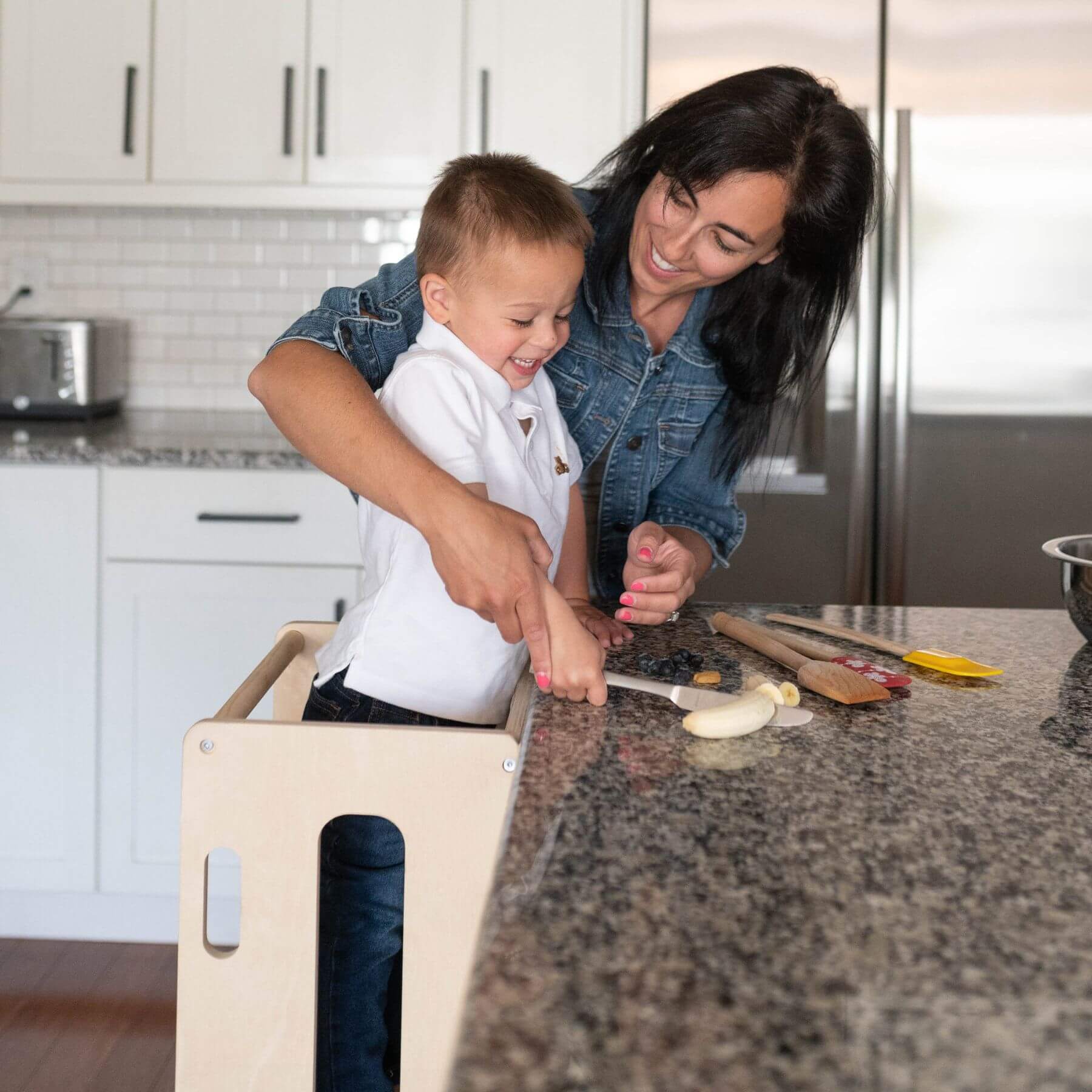 Mom Helping Kid Cutting Food, Kid Standing on Busy Kids 2-In-1 Kitchen Tower and Kids Art Desk