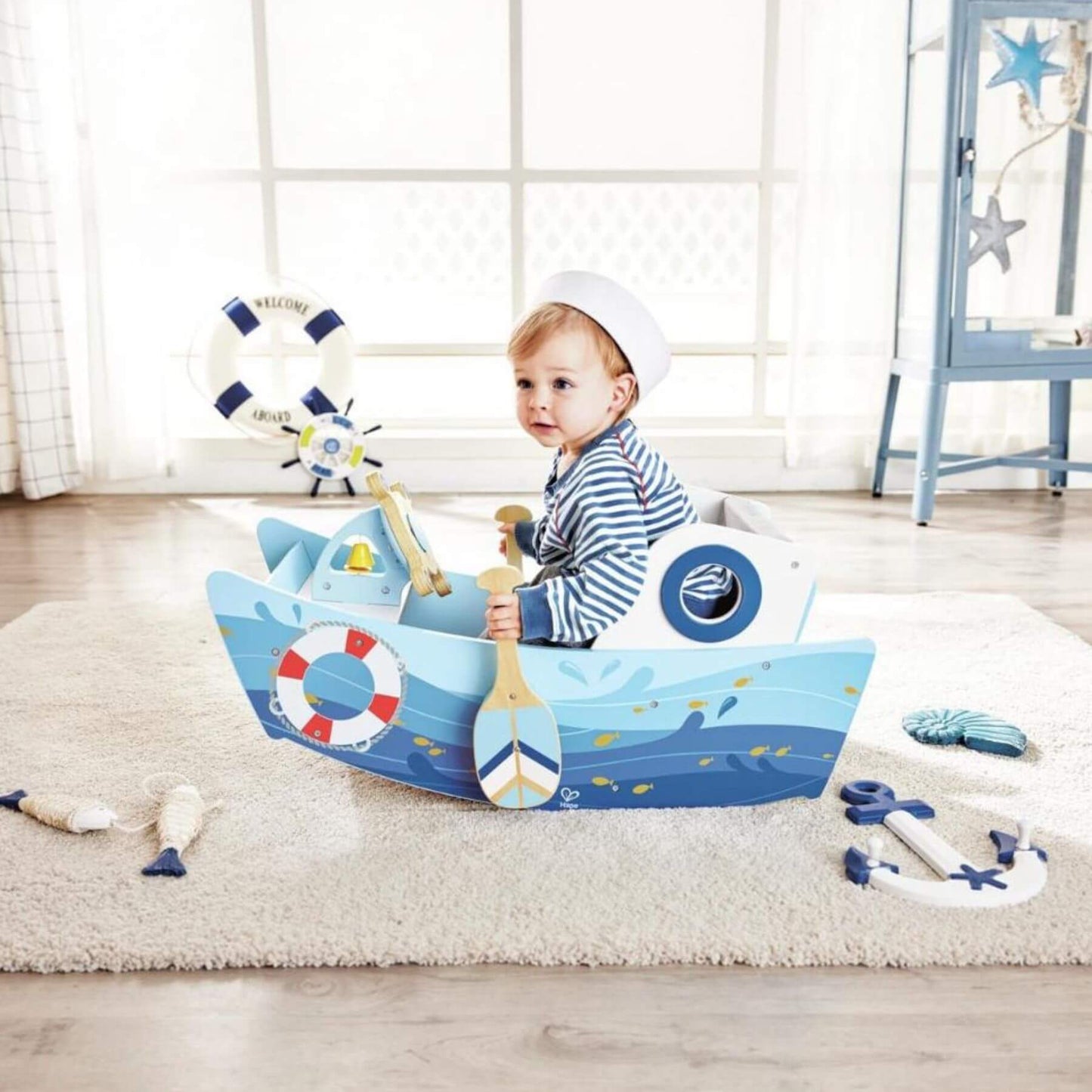 Child playing with Hape Captains Rocking Boat in a room with light wood flooring and white walls.