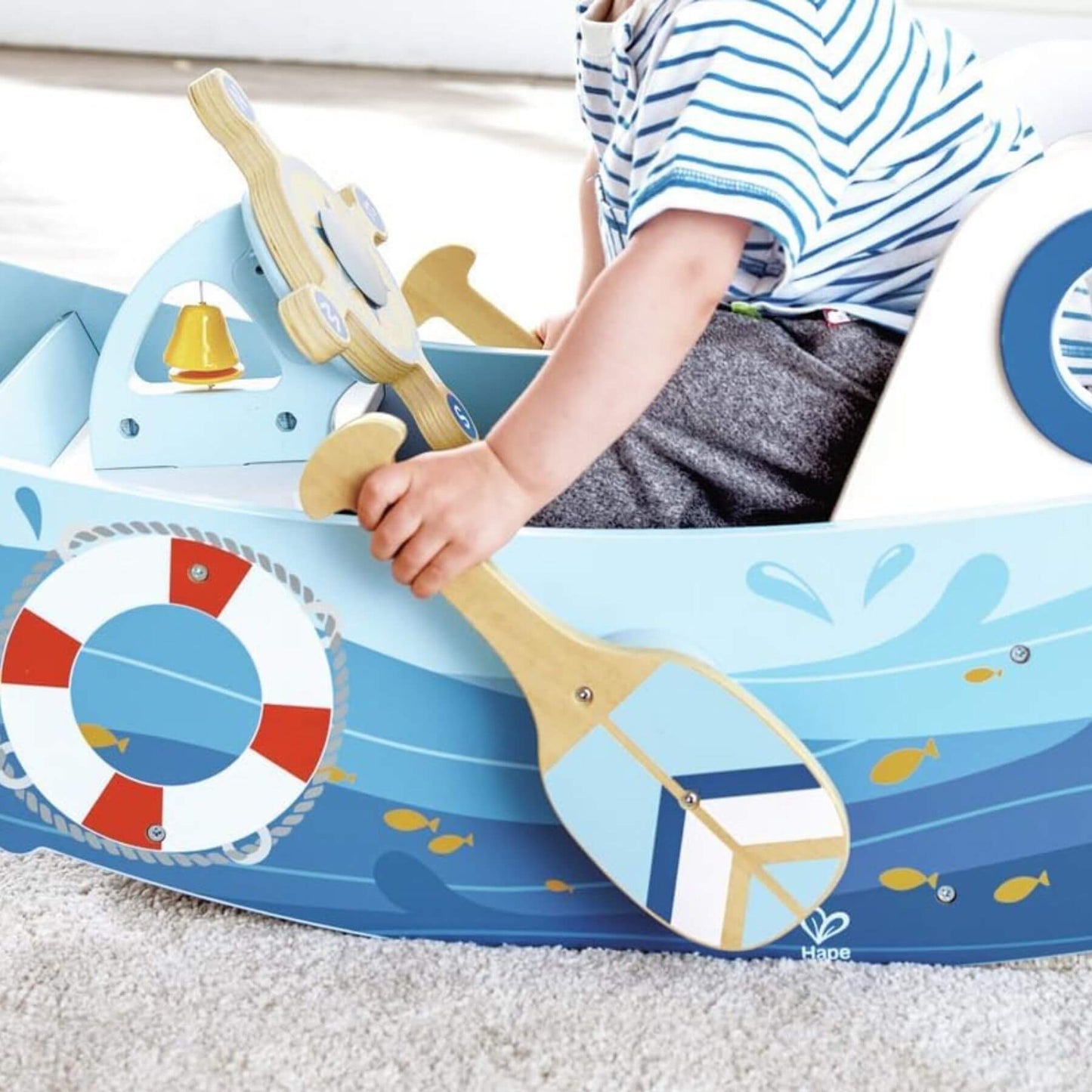 Child playing with Hape Captains Rocking Boat with paddles and nautical elements.