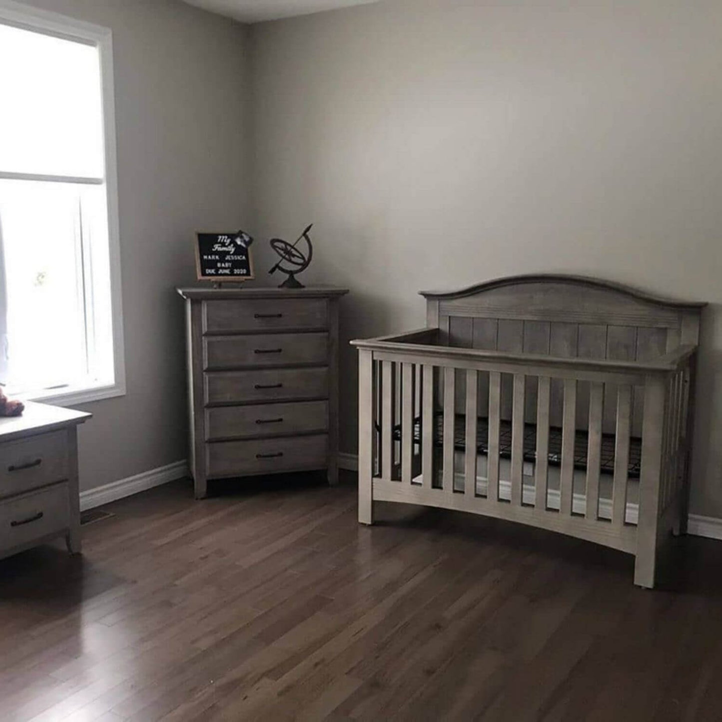Nursery room with wooden crib and dresser against a wall.