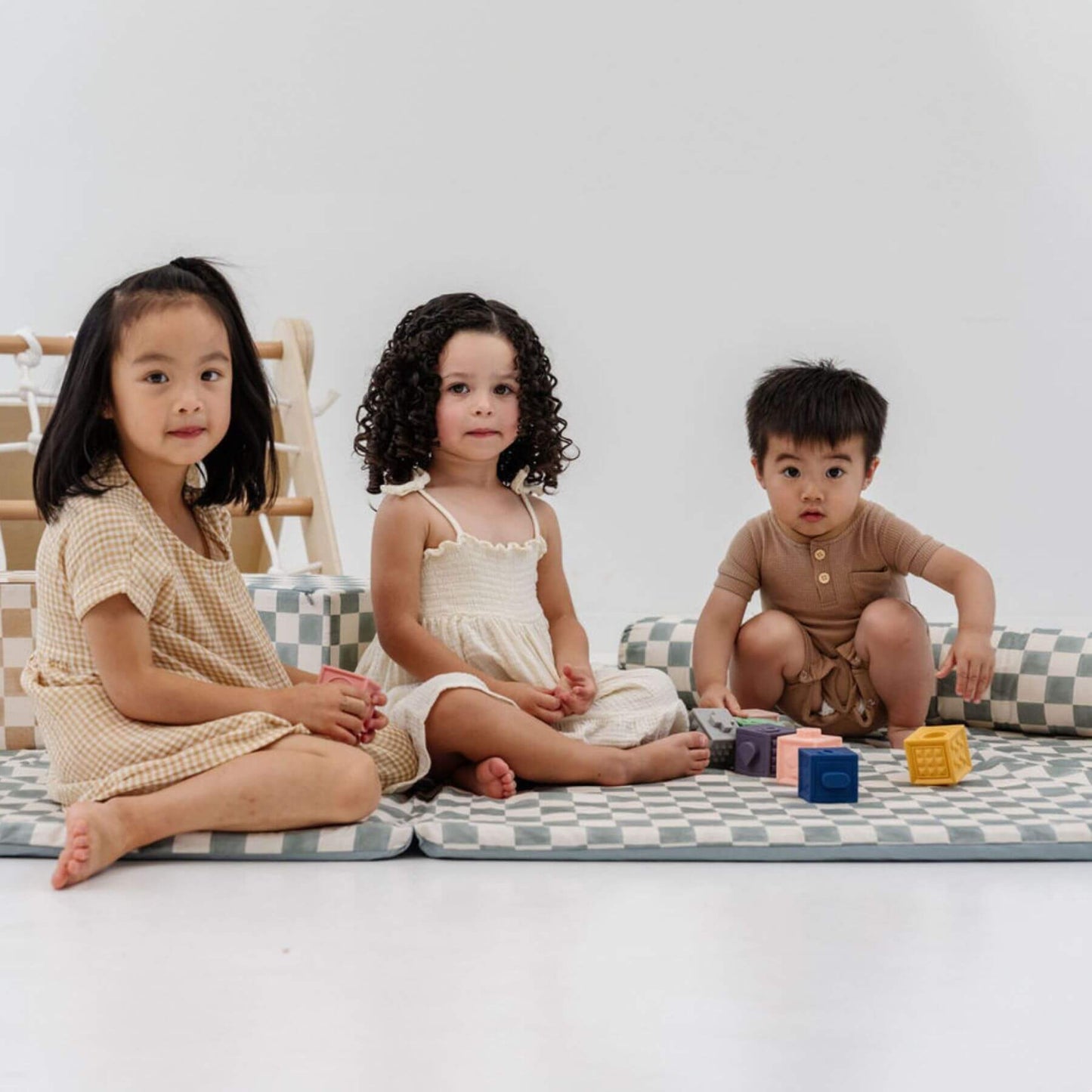 Three children sitting on Toki Kids Checker Matcha Organic Cotton Mat with colorful blocks around them.