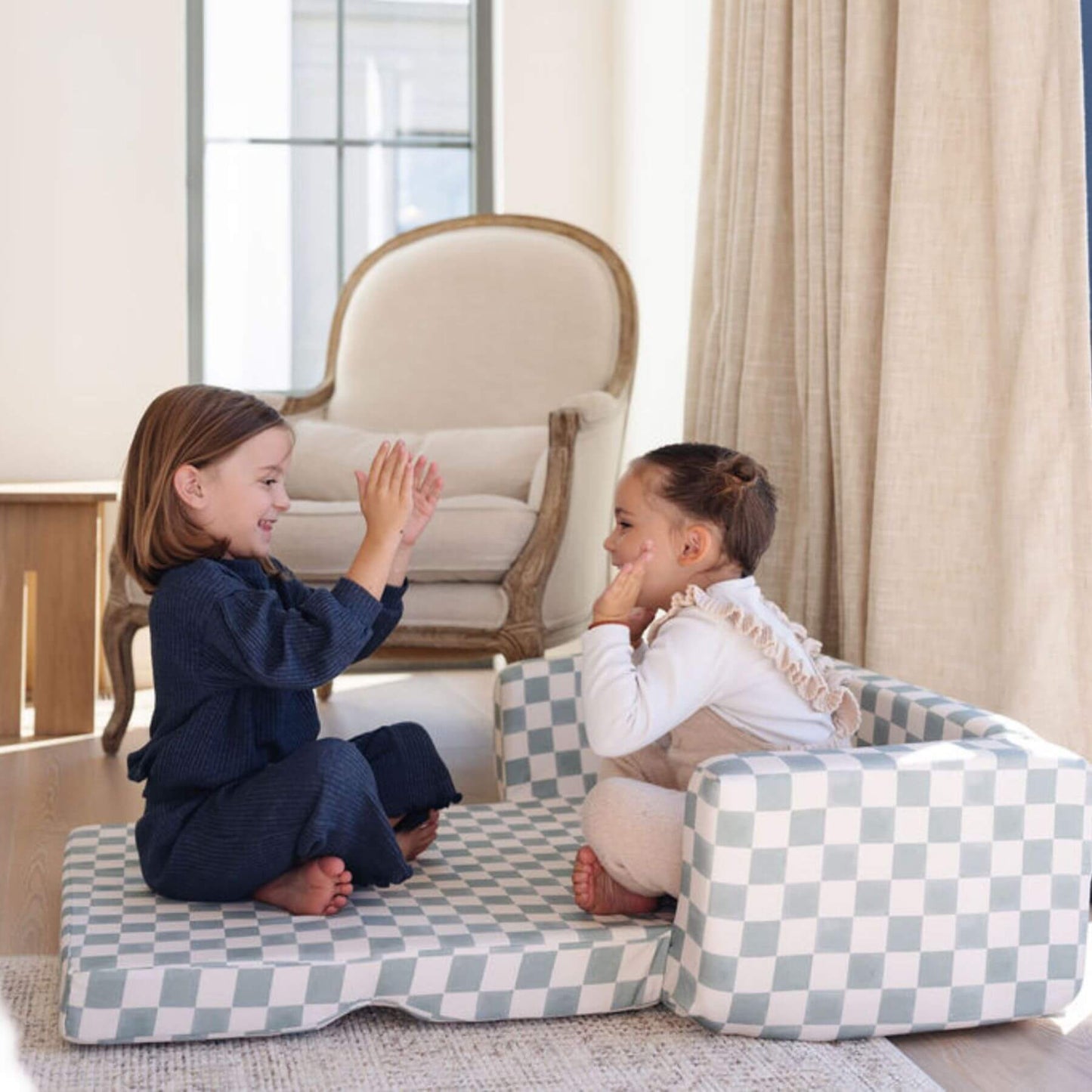 Two children playing on Toki Kids Checker Matcha Play Couch in a room with a chair and curtains.