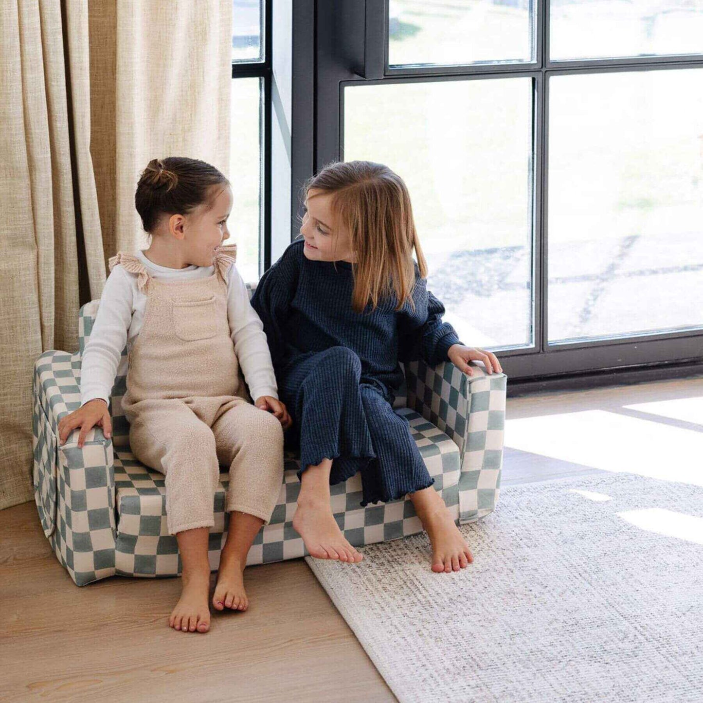 Two children sitting on Toki Kids Checker Matcha Play Couch in a bright room with large windows.
