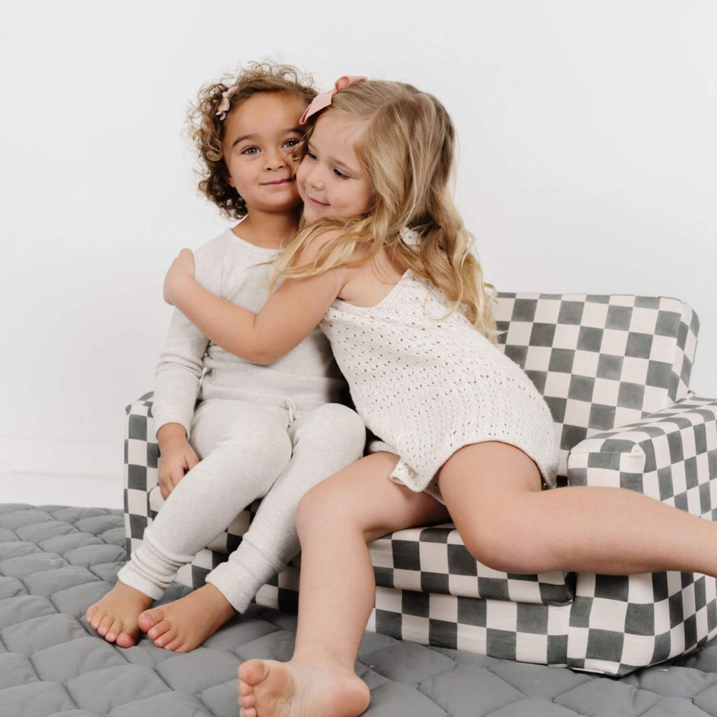 Two young girls sitting on Toki Kids Checker Pepper Play Couch, wearing matching white outfits.