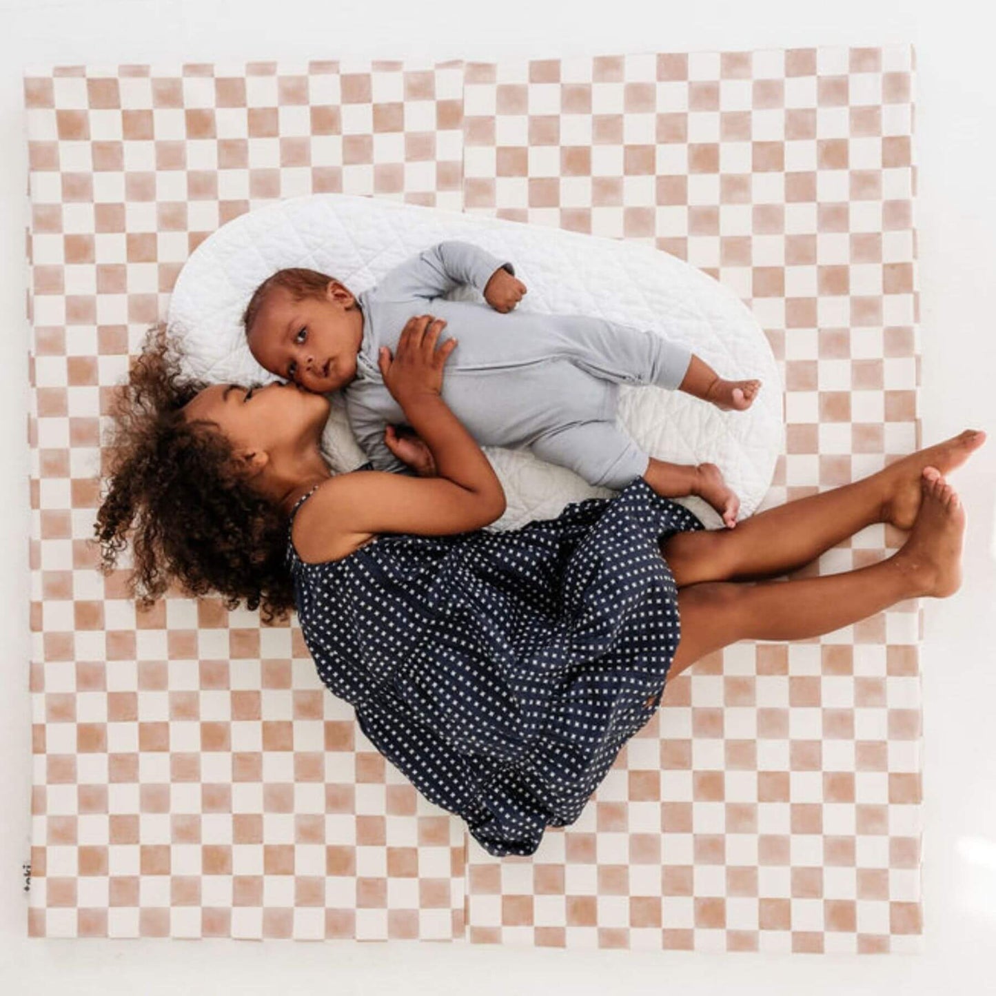 Two children lying on Toki Kids Checker Toffee Vegan Leather Mat, one holding the other.