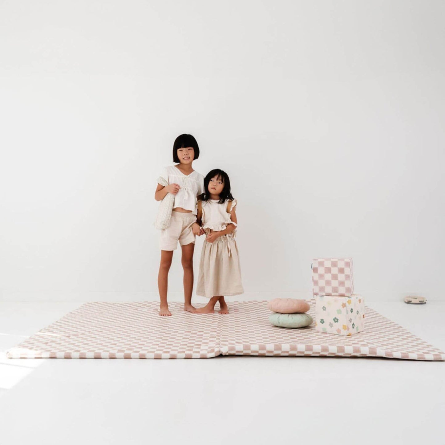 Two children standing on Toki Kids Checker Toffee Vegan Leather Mat with colorful pillows against a white background