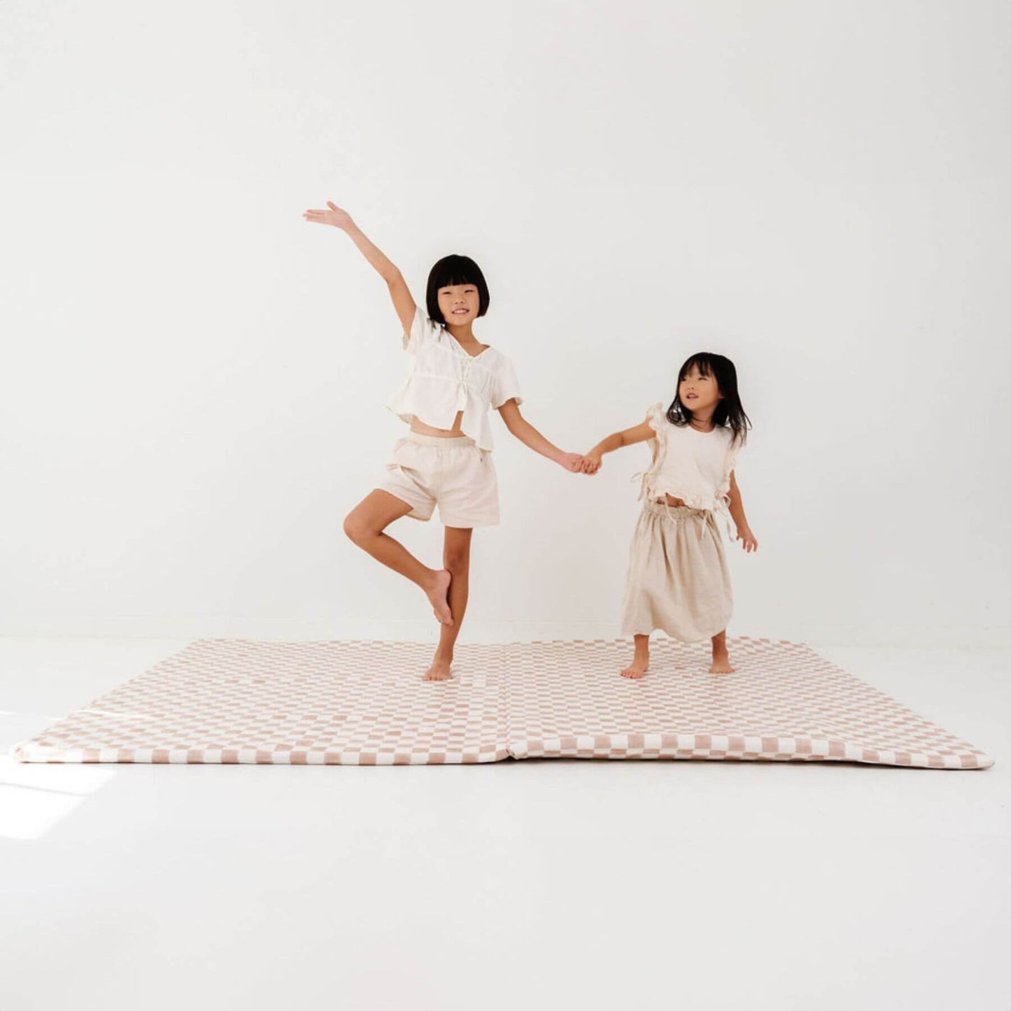 Two children holding hands on Toki Kids Checker Toffee Vegan Leather Mat against a white background