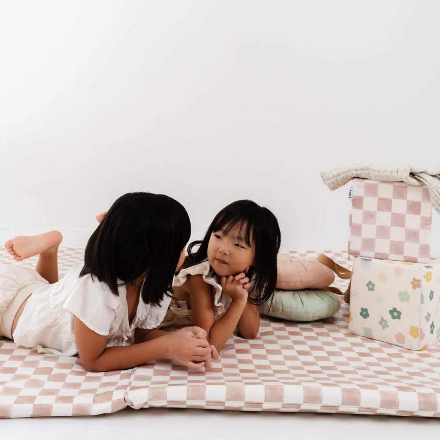 Two children lying on Toki Kids Checker Toffee Vegan Leather Mat with pillows
