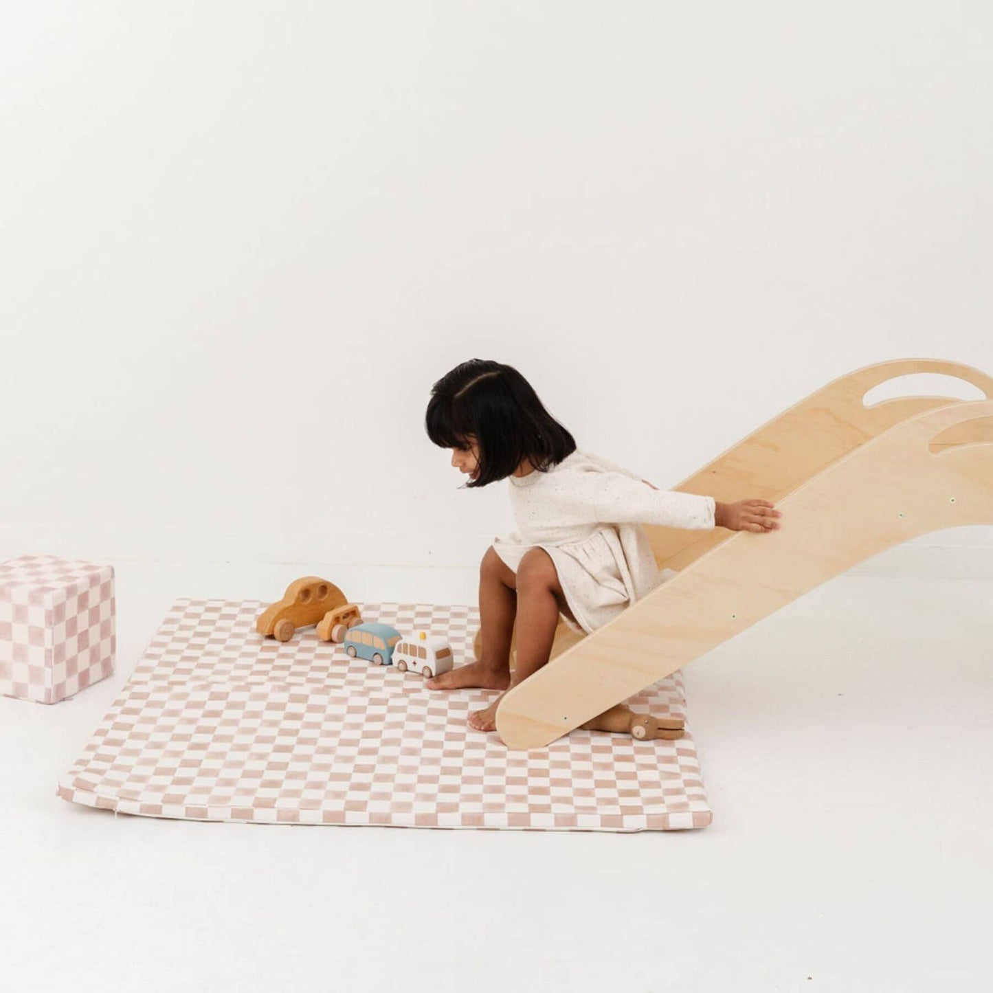 Child playing with a wooden slide and Toki Kids Checker Toffee Vegan Leather Mat on a white floor.