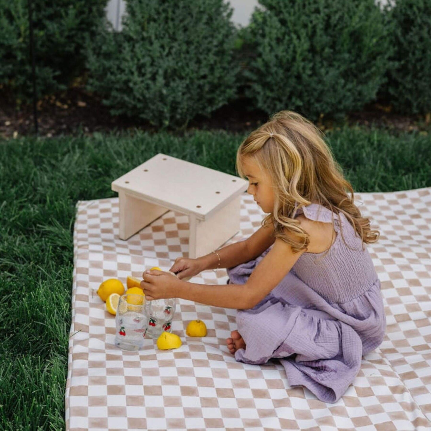 Child playing with lemons and a small stool on Toki Kids Checker Toffee Vegan Leather Mat outdoors.