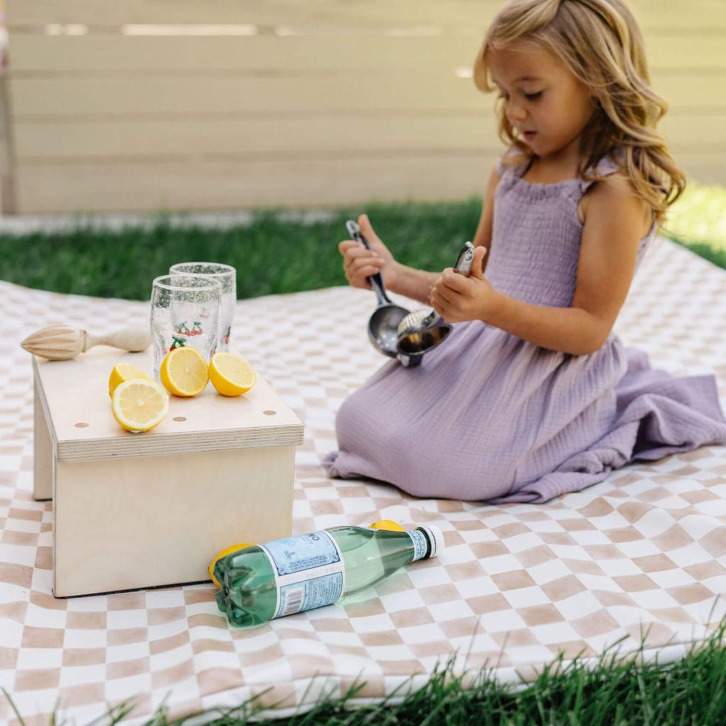Child in a purple dress sitting on Toki Kids Checker Toffee Vegan Leather Mat with lemons, glasses, and a bottle.