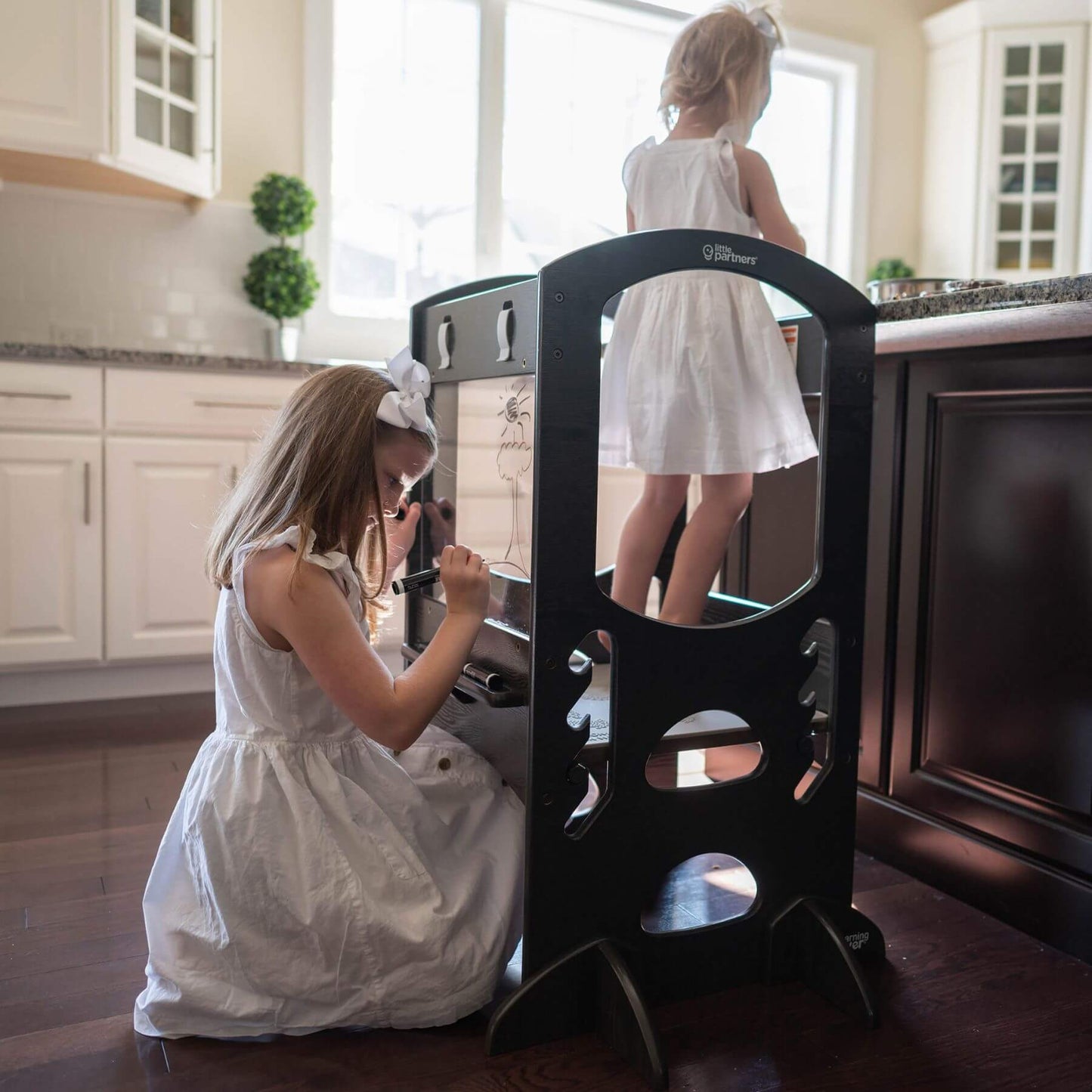 Girl Standing on Little Partners Chef Series Learning Tower Charcoal, with Sibling Drawing on plexi-glass panel