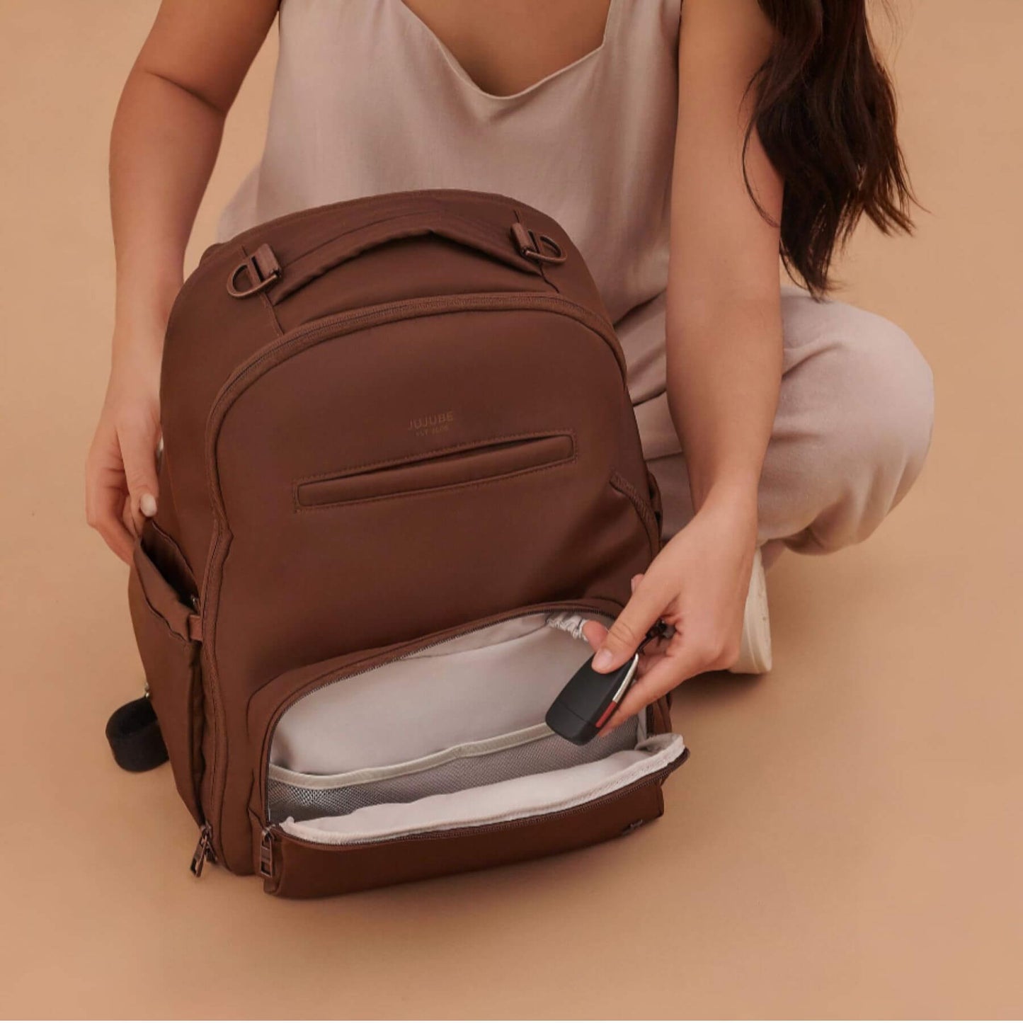 Person opening JuJuBe Classic Diaper Backpack Espresso on a beige background
