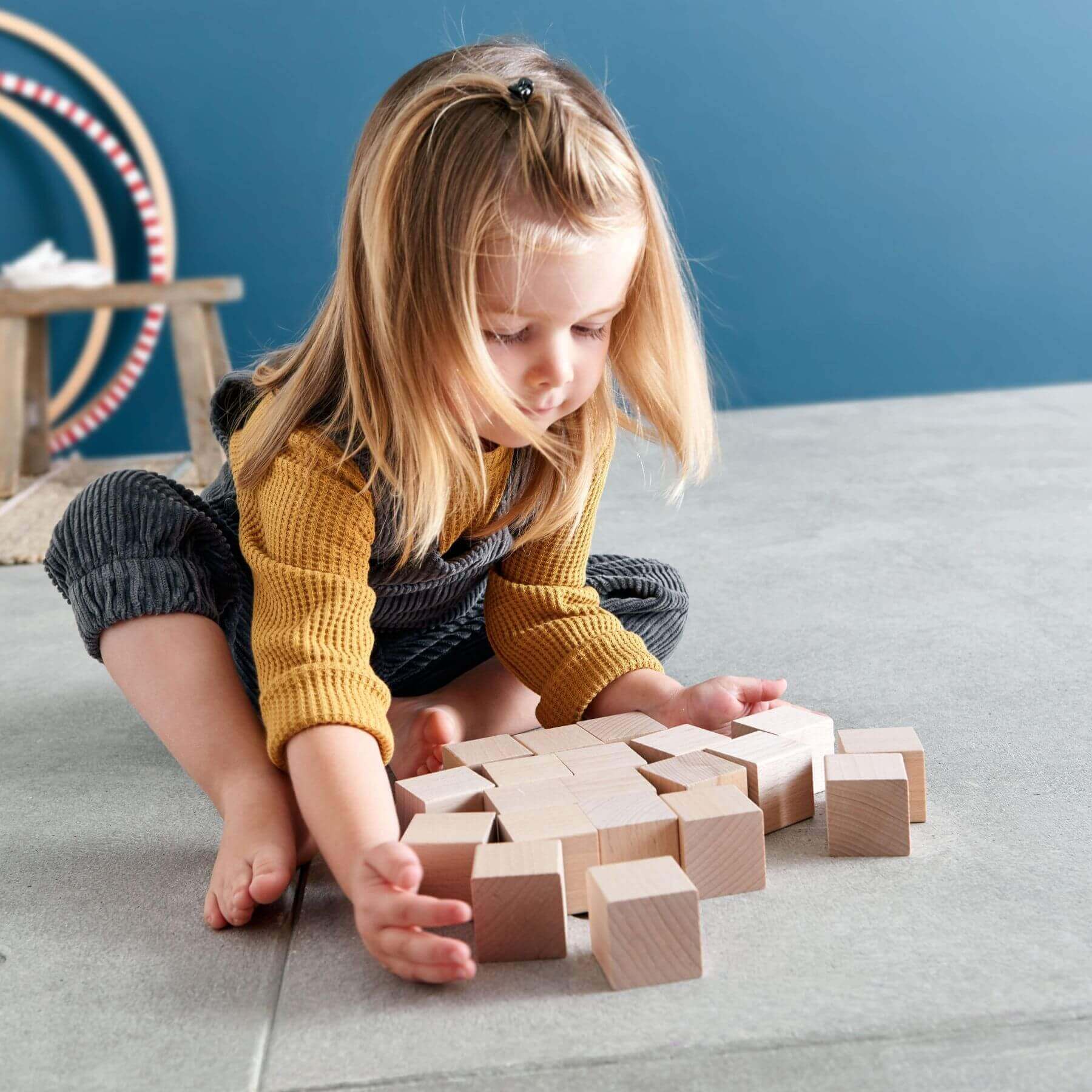 Child playing with wHABA USA Clever Up! Building Block System 2.0 on a carpeted floor against a blue wall.