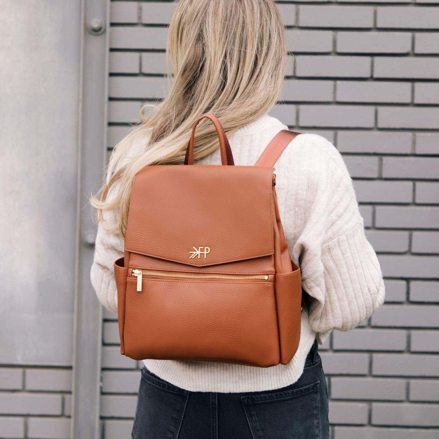 Person wearing Cognac Mini Classic Bag II with a brand logo against a brick wall.