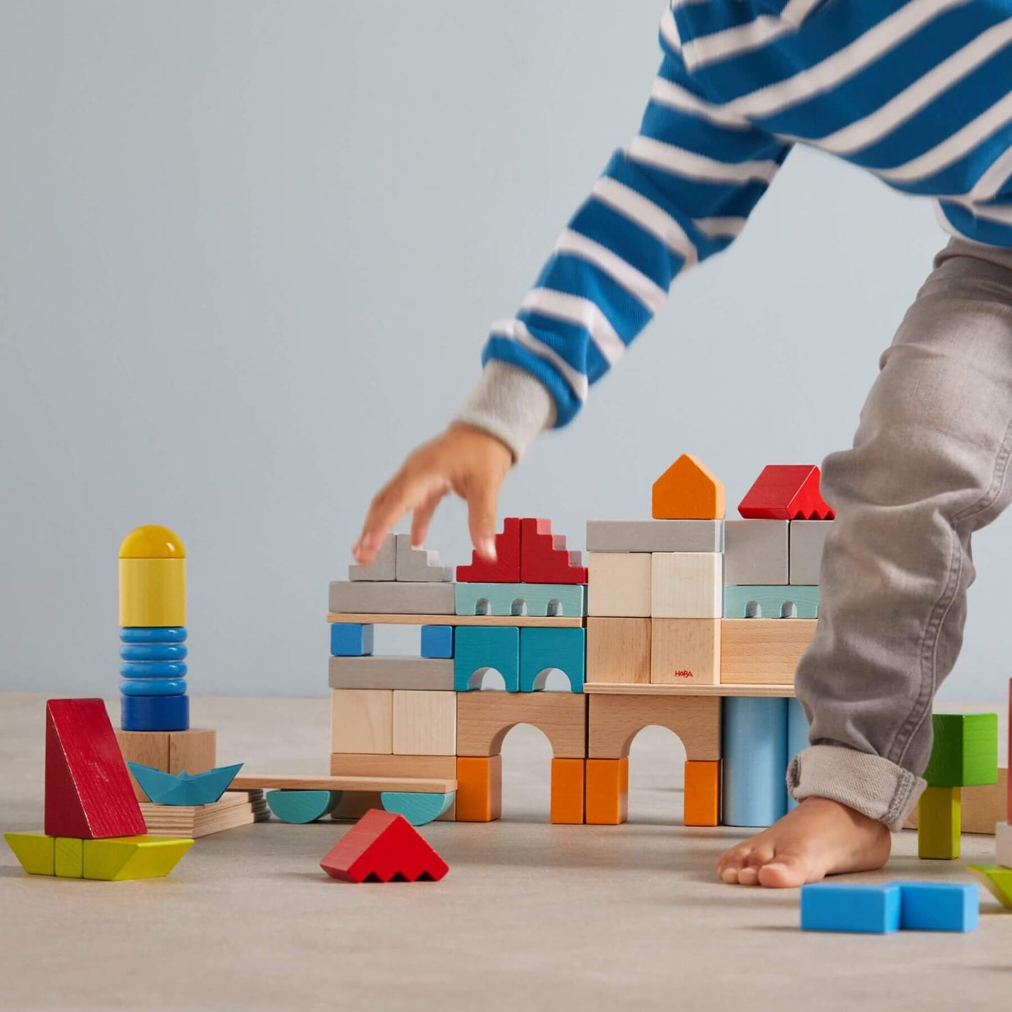 Child playing with HABA USA Colored Wooden Building Blocks - 85 Piece Set on a wooden floor.