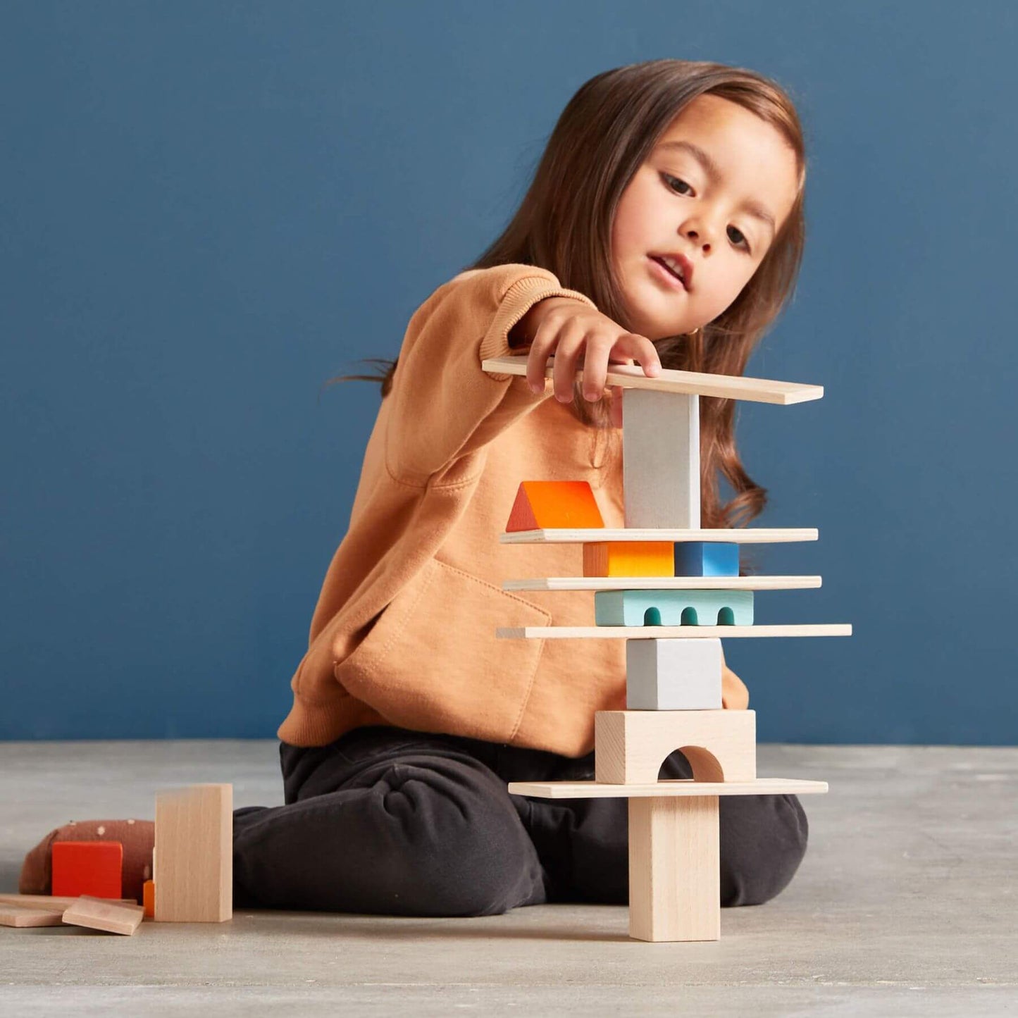 Child playing with HABA USA Colored Wooden Building Blocks - 85 Piece Set against a blue background