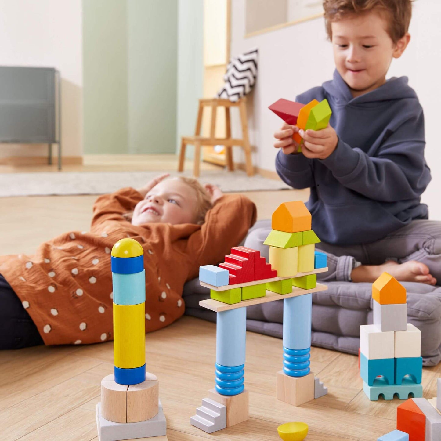 Two children playing with HABA USA Colored Wooden Building Blocks - 85 Piece Set on a wooden floor.