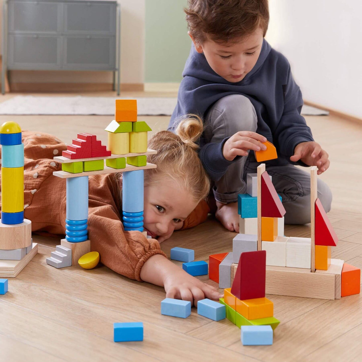 Two children playing withHABA USA Colored Wooden Building Blocks - 85 Piece Set on a wooden floor.