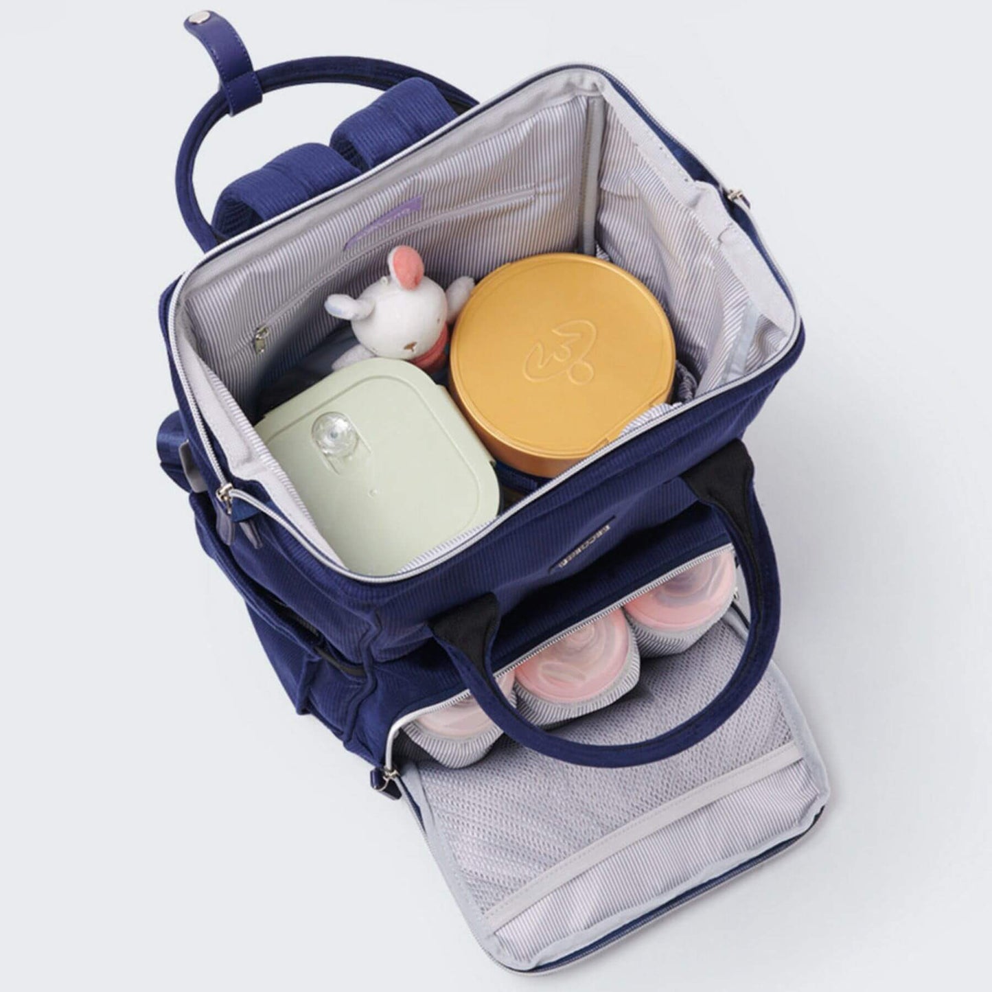 Corduroy Diaper Backpack Blue with baby items including a yellow container, pink shoes, and a white toy