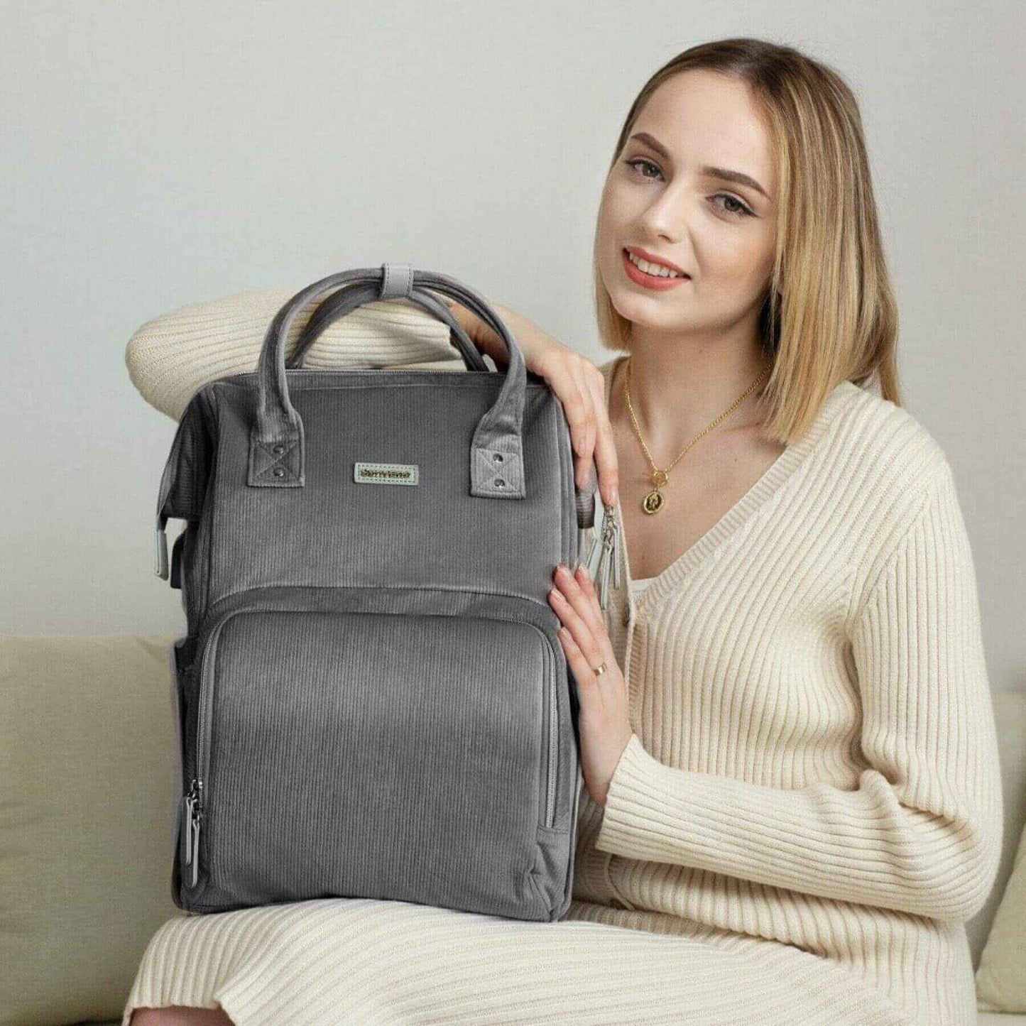 Woman holding Corduroy Diaper Backpack Grey, sitting on a couch.